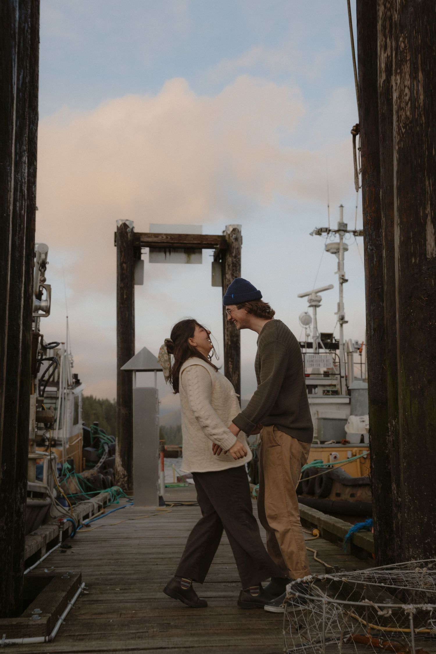 People engage in conversation on a wooden pier with boats and mountains visible in the distance.