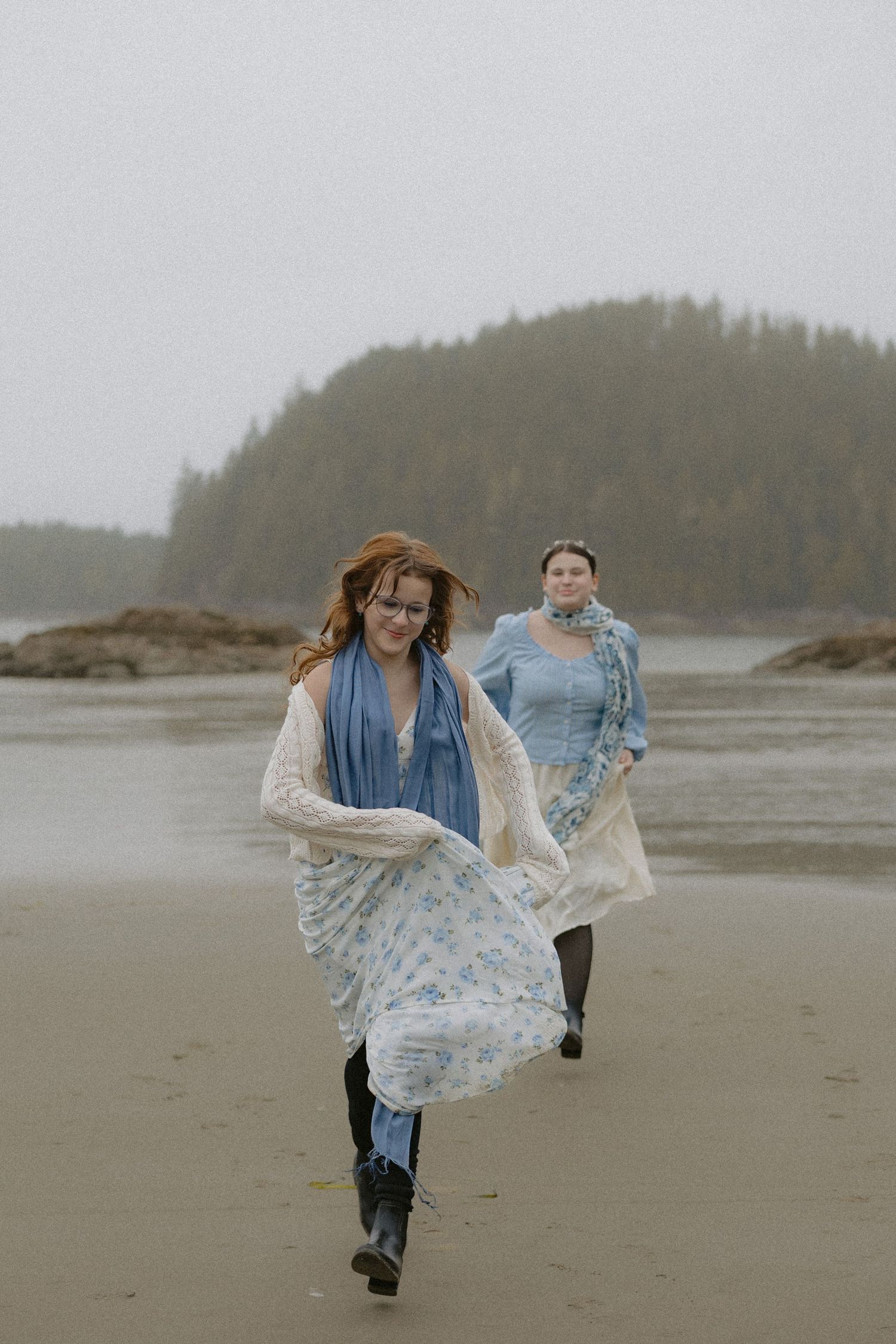 A person in a flowing dress runs joyfully across a foggy beach landscape.