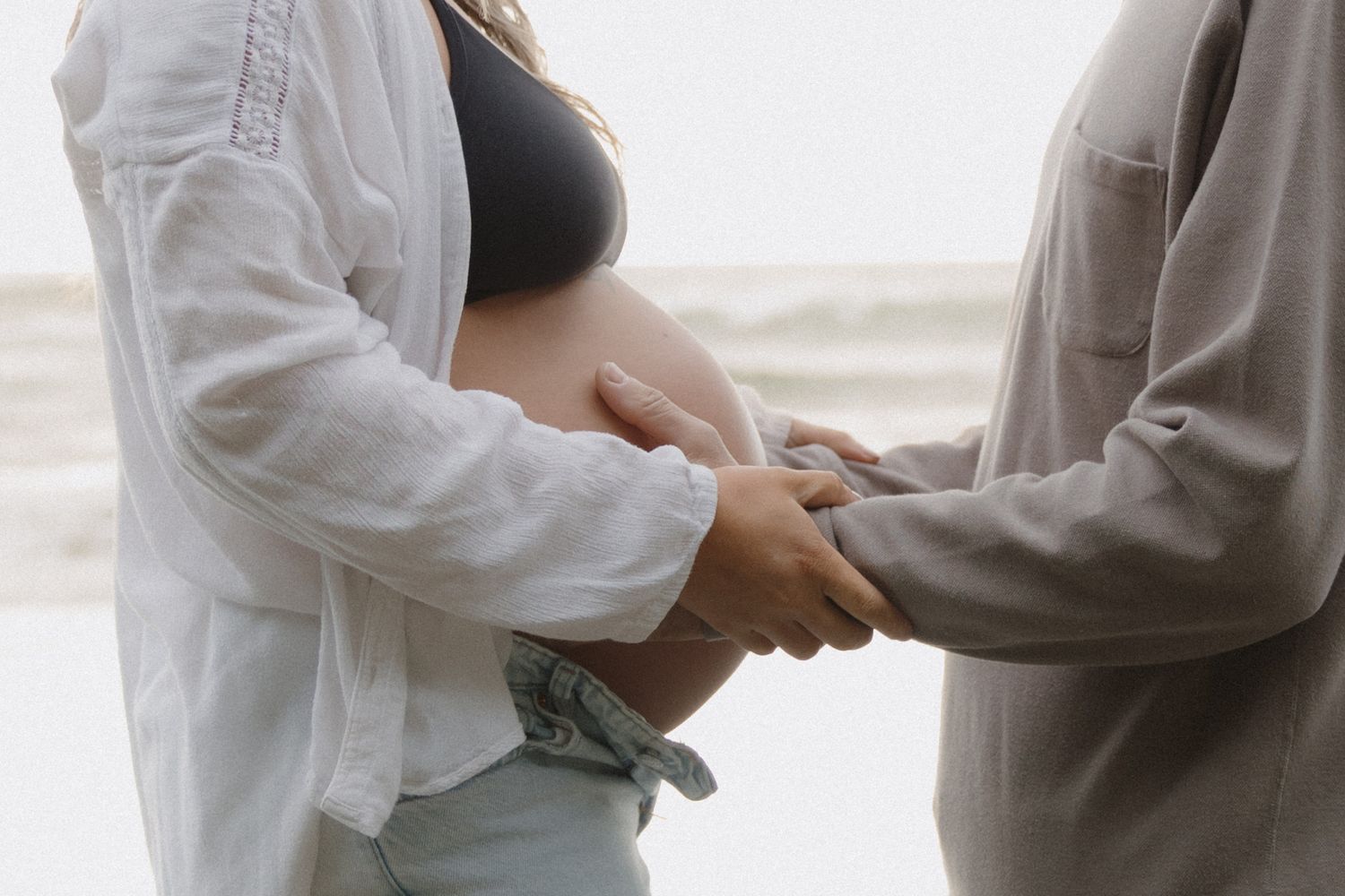 Close-up of couple holding hands during beach maternity session.