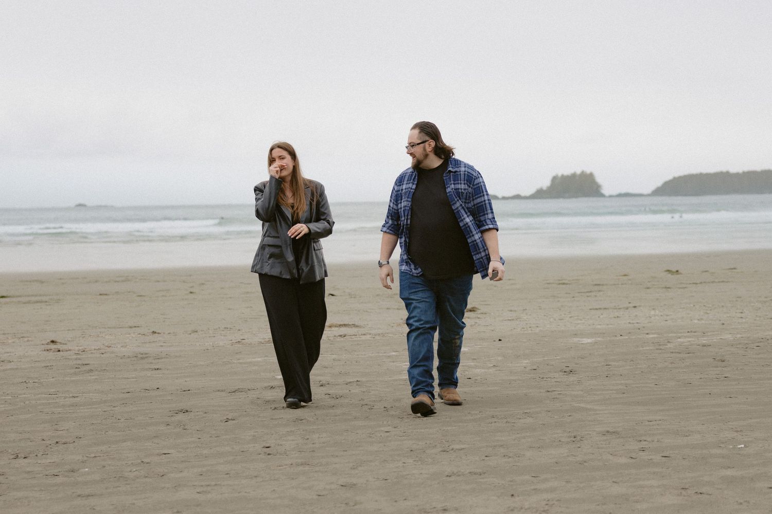 A couple strolls along a deserted beach on an overcast day.