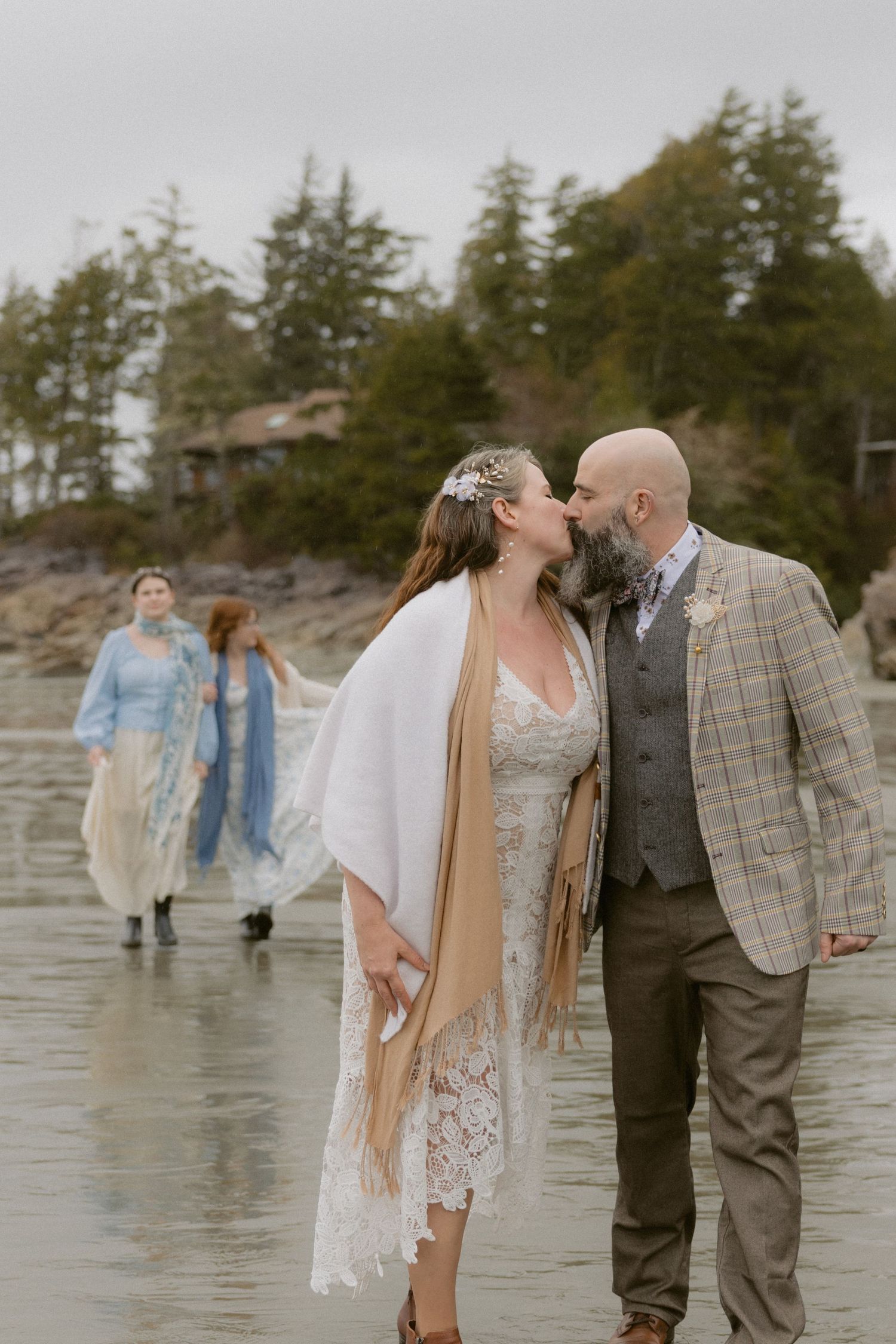 Intimate wedding ceremony moment on moody Pacific Northwest beach with evergreens in background.
