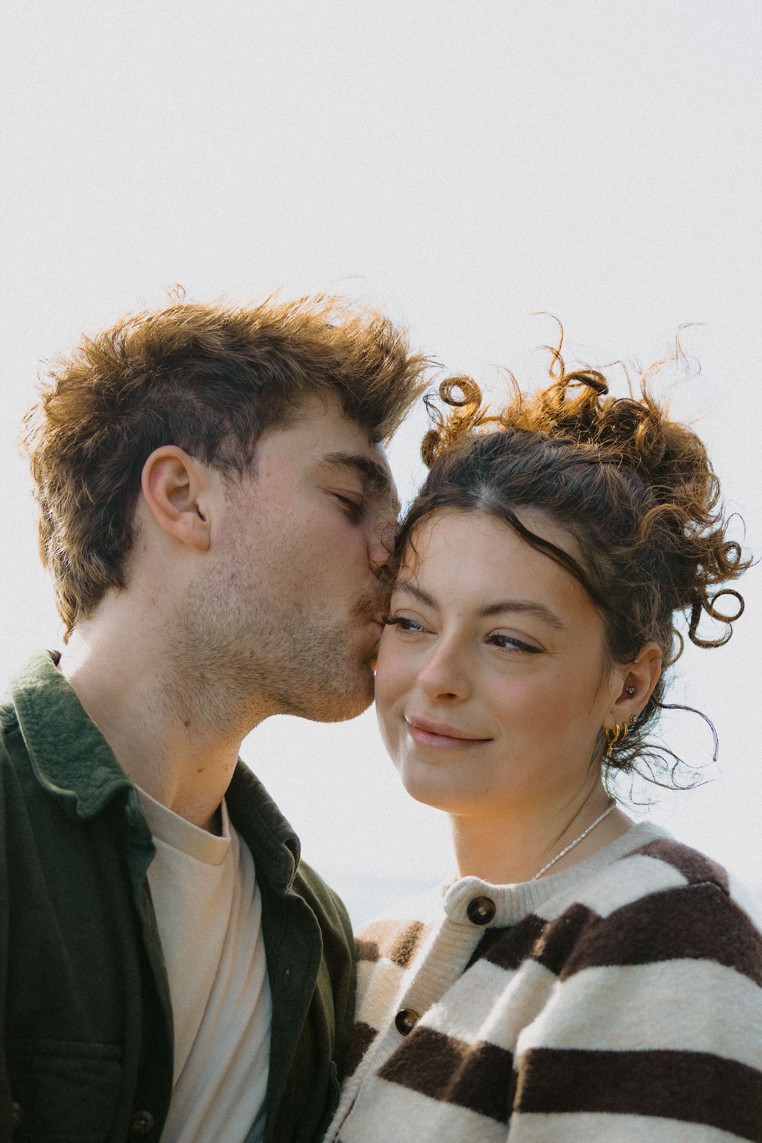 A young couple sharing a tender moment as the man gently kisses the woman on the cheek outdoors.