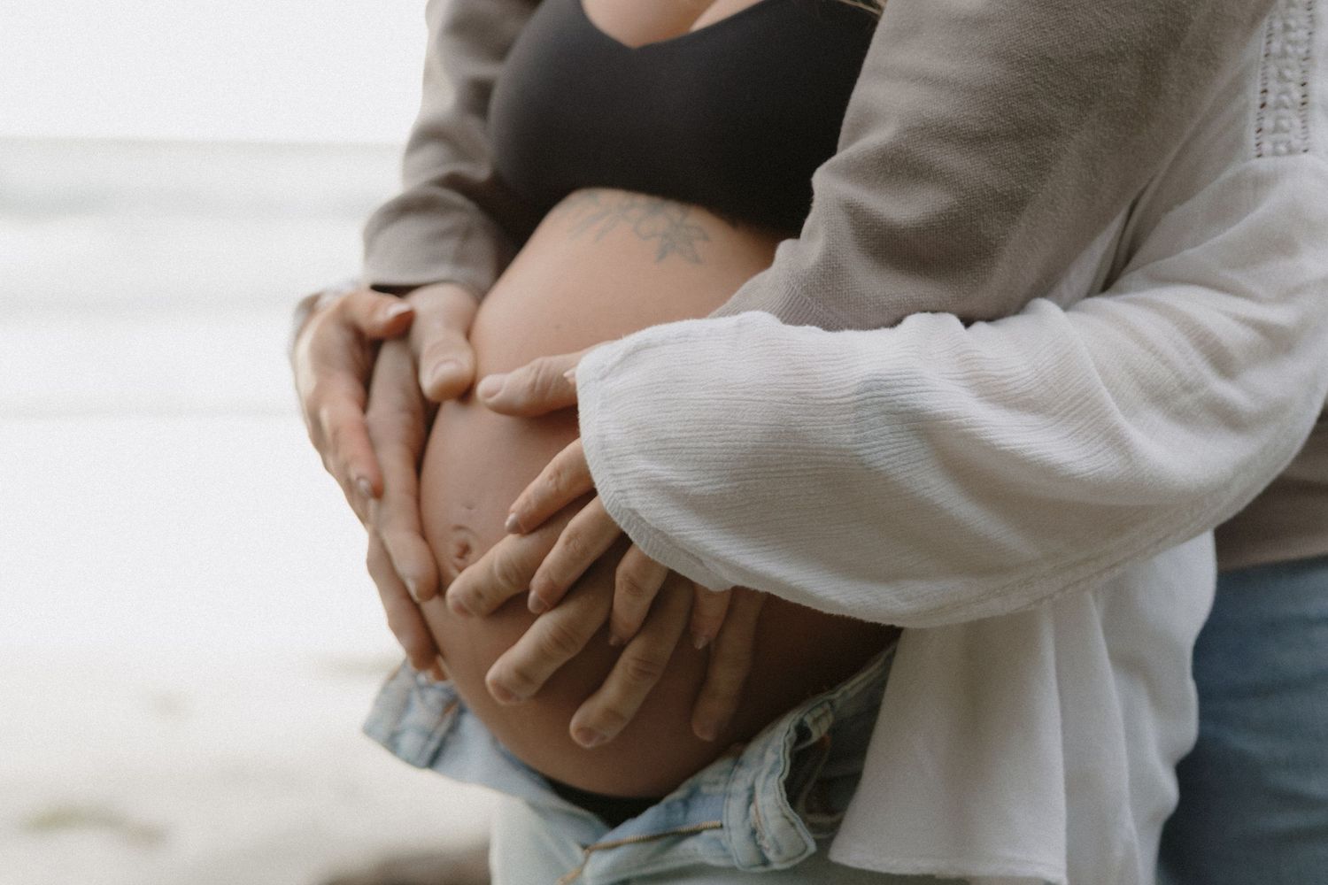 A couple embraces tenderly on a misty beach during a maternity photoshoot.