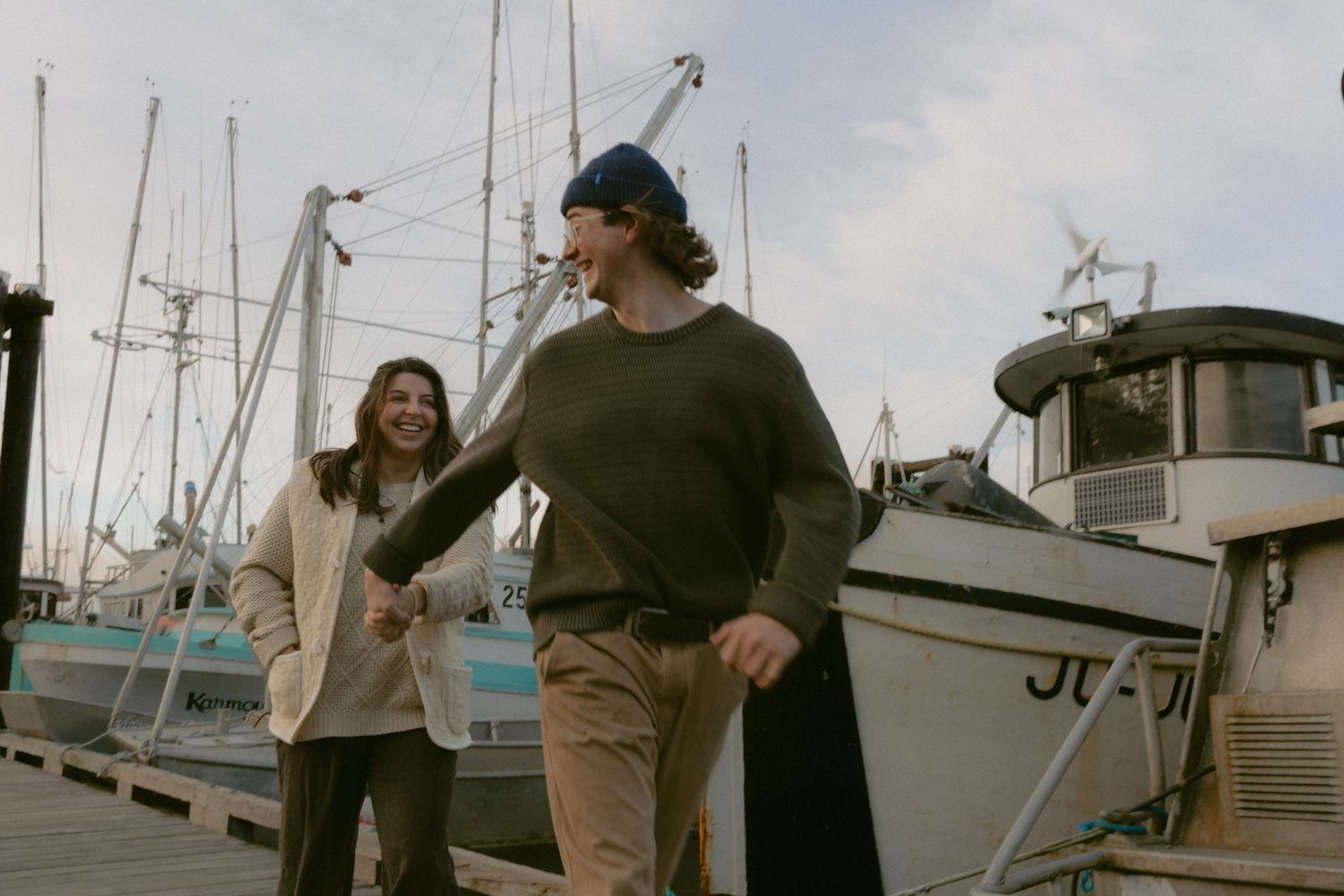People strolling along a wooden pier surrounded by docked boats on a cloudy day.
