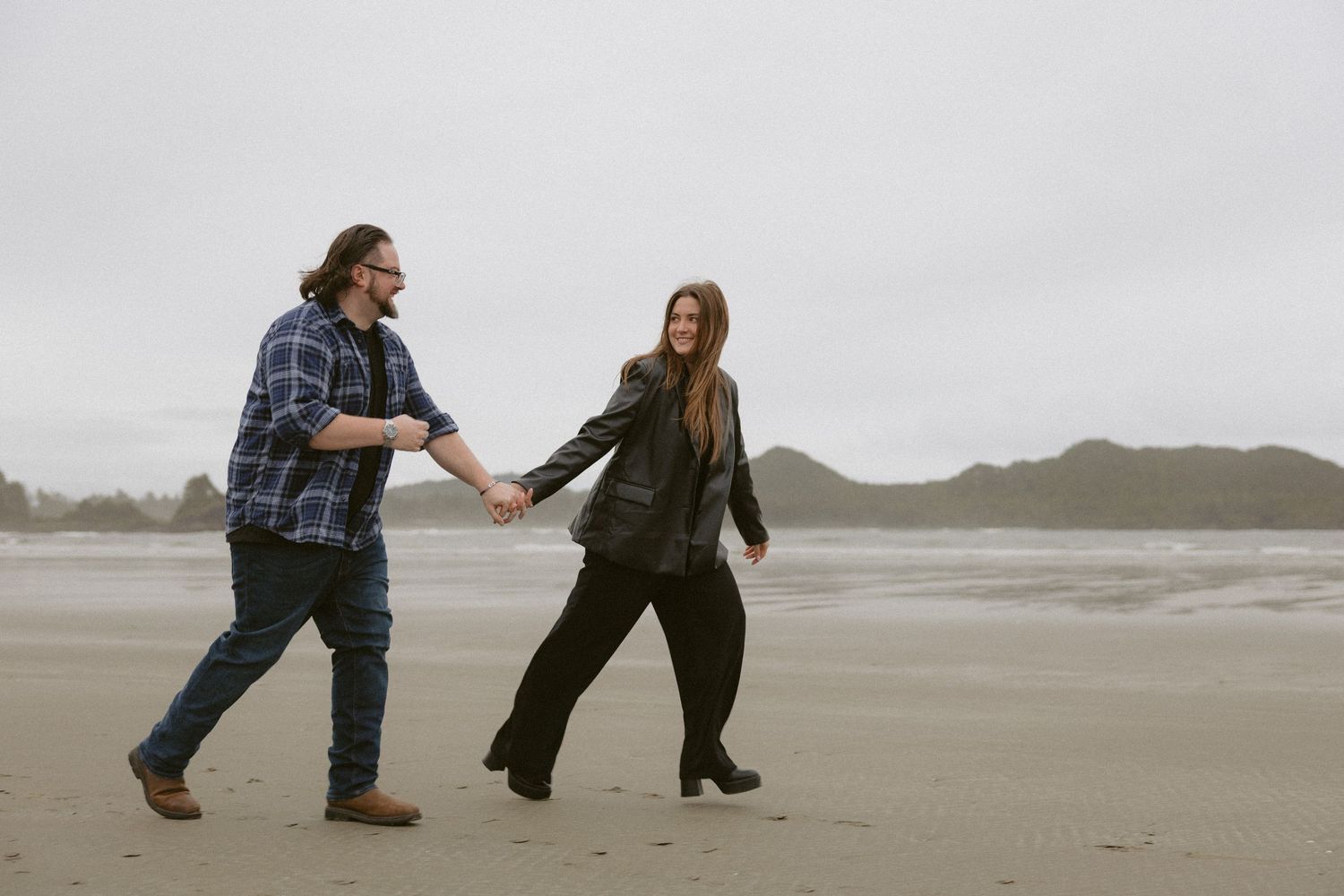 Couple dancing playfully on an empty beach during an overcast day