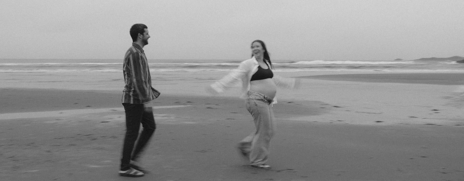 Black and white photo of couple dancing on beach during maternity shoot.