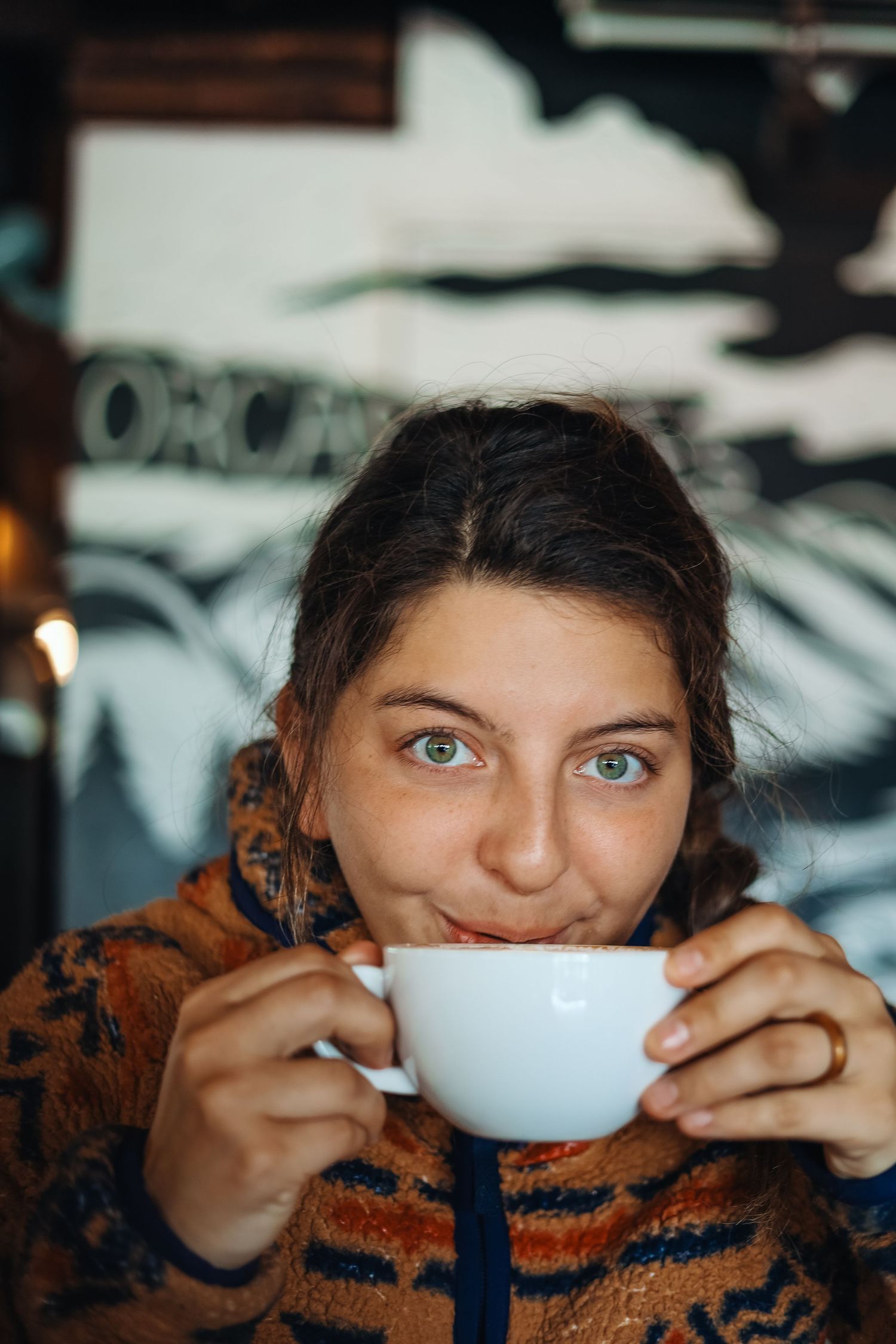 Tofino wedding photographer Mariana sipping from white coffee cup while wearing cozy orange striped sweater