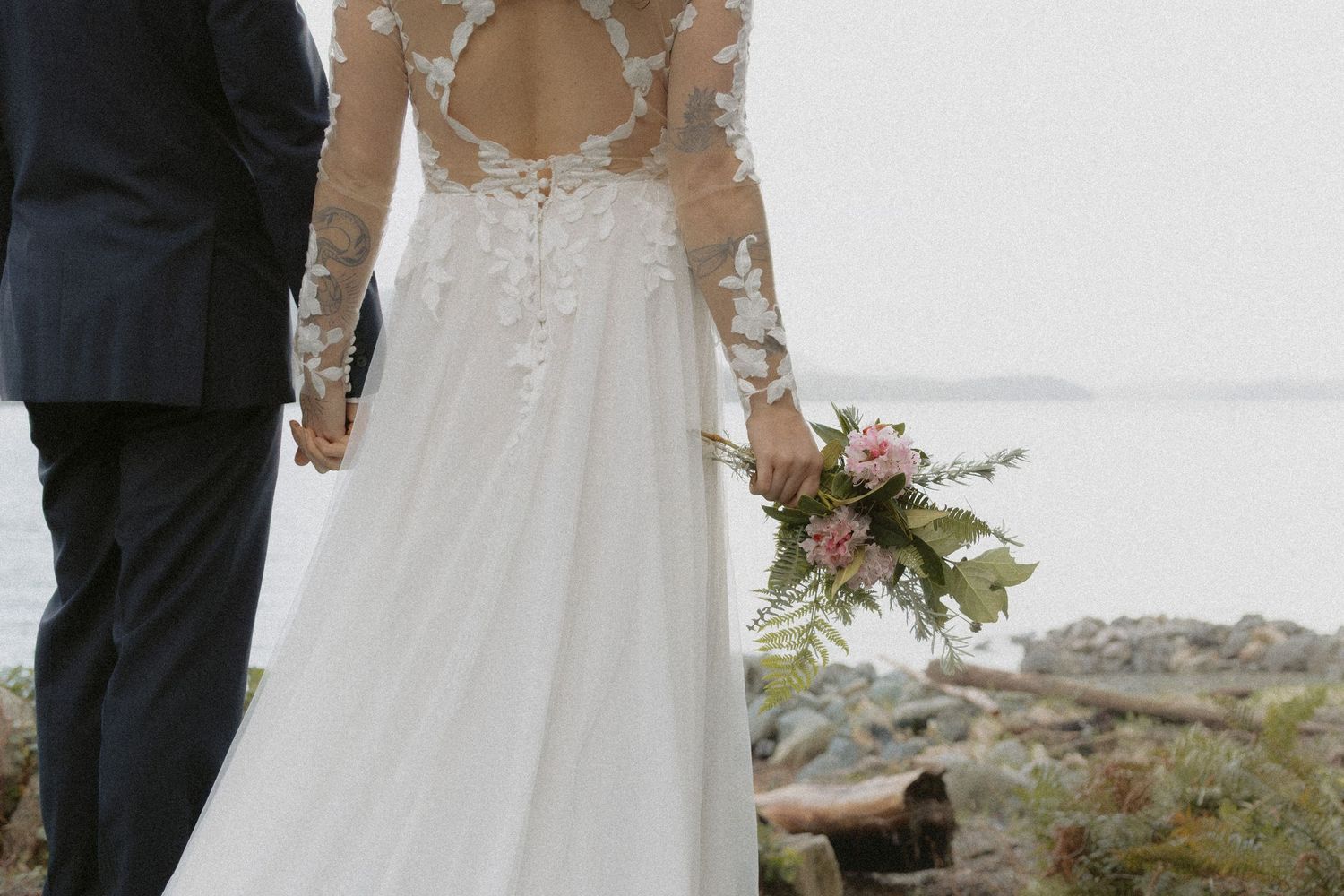 A couple in wedding attire standing together against a scenic coastal backdrop.