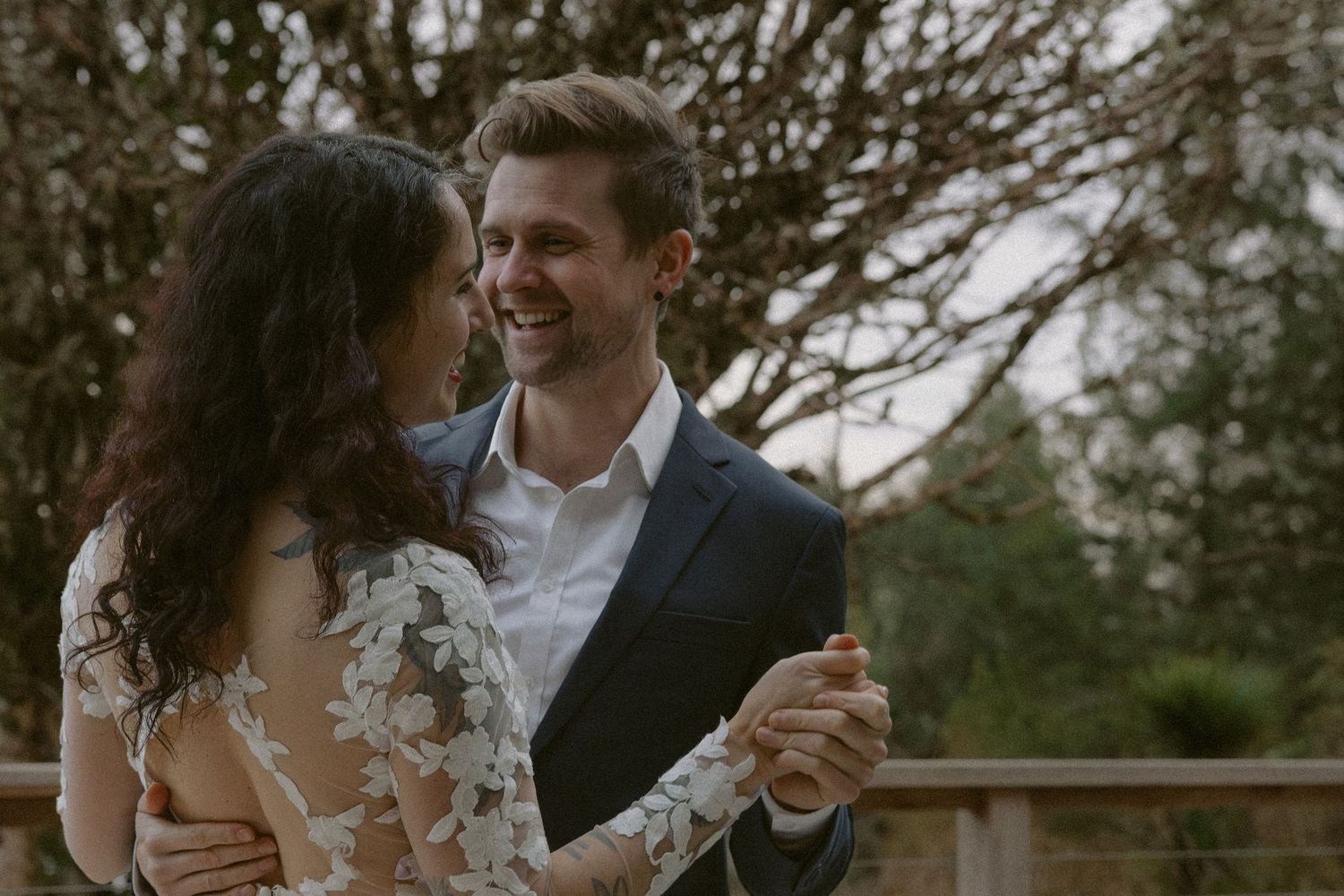 A couple shares a tender moment while dancing on a deck surrounded by evergreen trees and mountains.