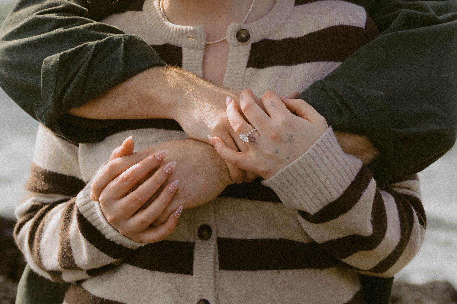 Close-up of couple embracing showing engagement ring on womans hand against striped sweater.