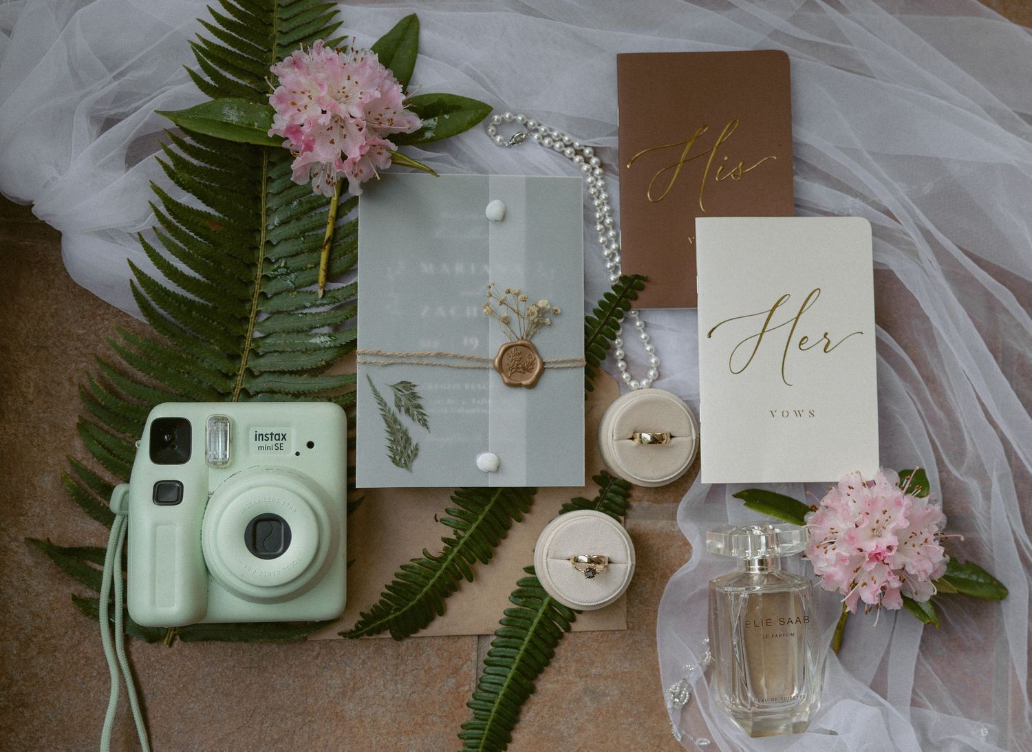 Tofino wedding details flat lay with ferns, pink flowers, and a mint green instant camera