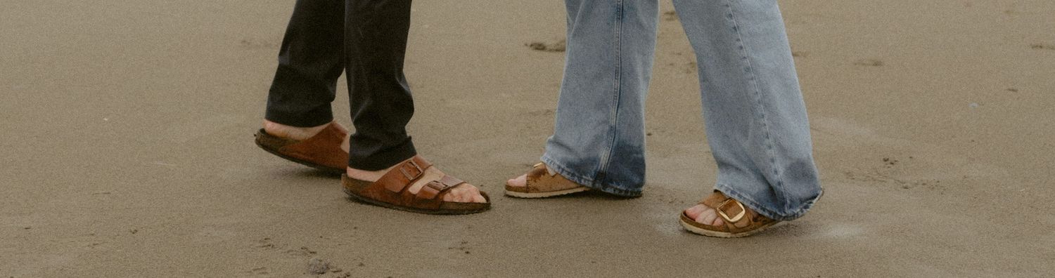 A close-up view of feet and legs of people standing in casual shoes and jeans on a concrete surface.