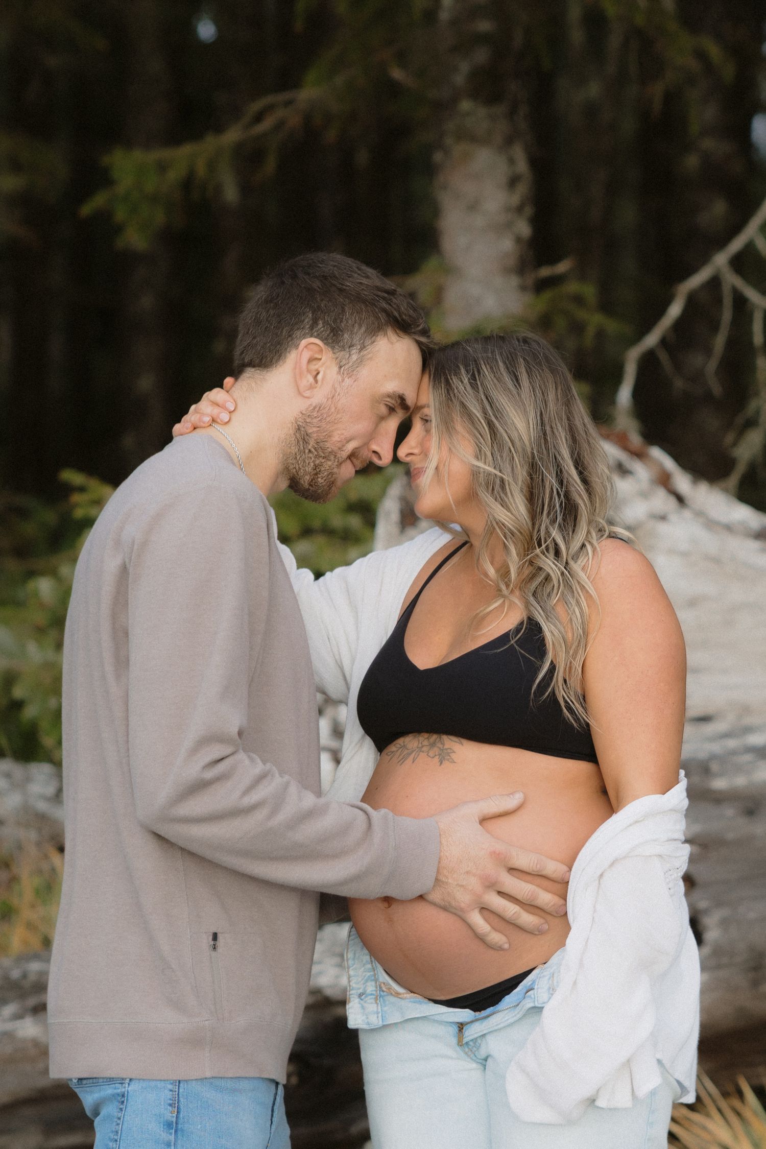 Tender moment between couple during forest maternity photoshoot.