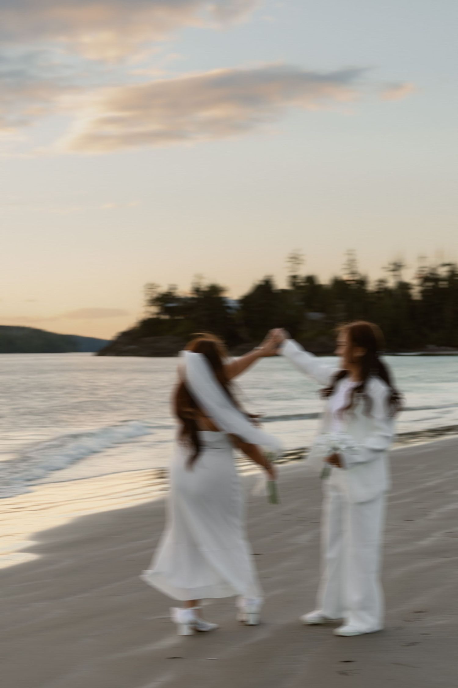 A joyful moment captured on the beach as two people in white dance together at sunset.
