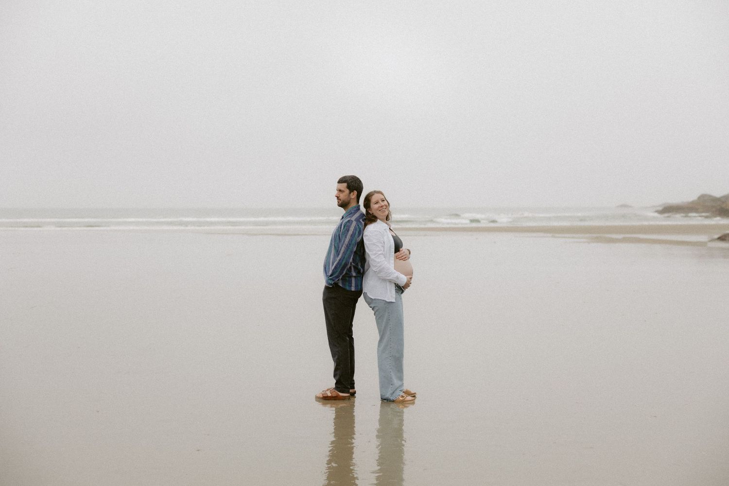 Two people share an intimate moment while standing on a foggy shoreline.
