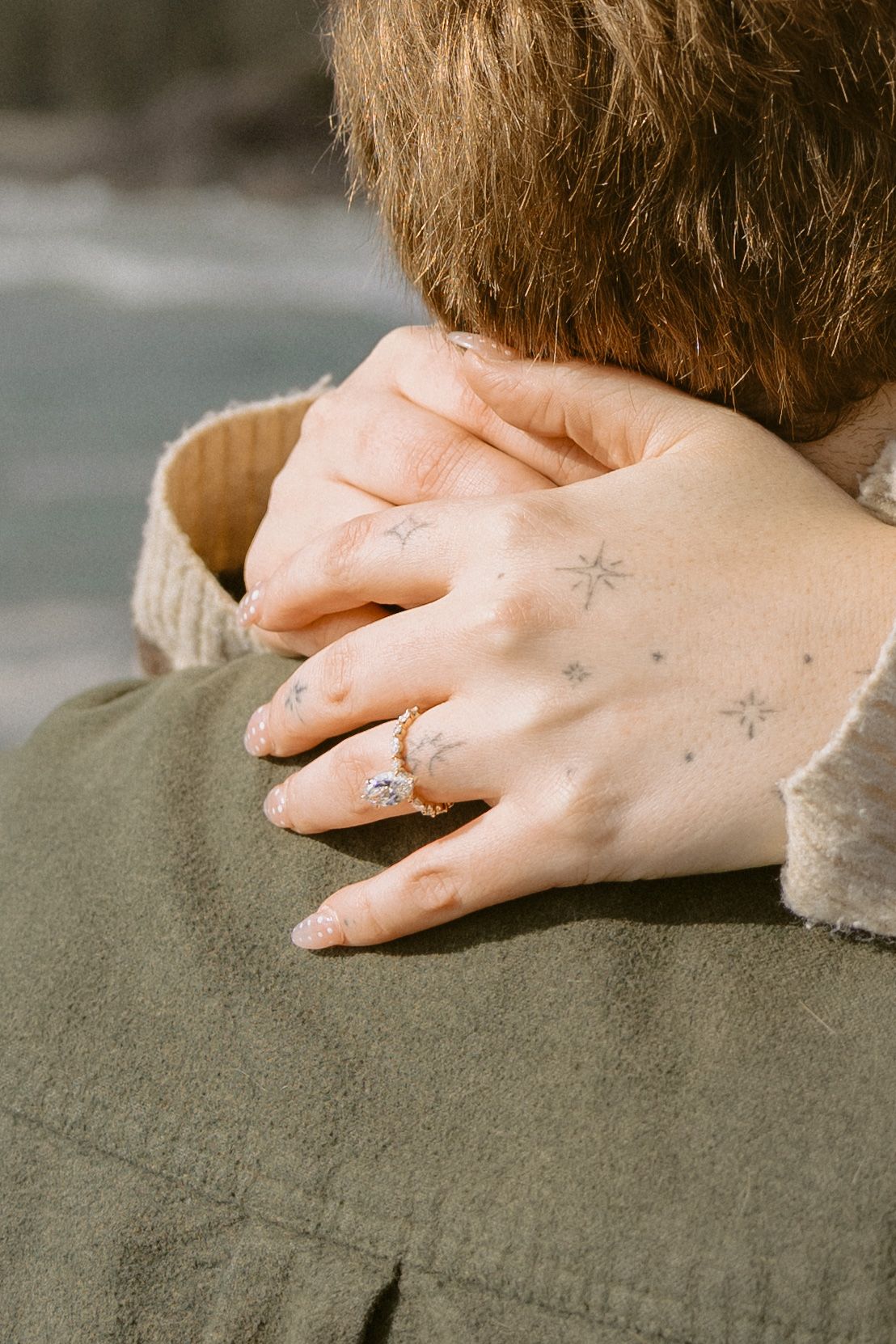 Close-up of womans hand with engagement ring and star tattoos resting on mans shoulder.