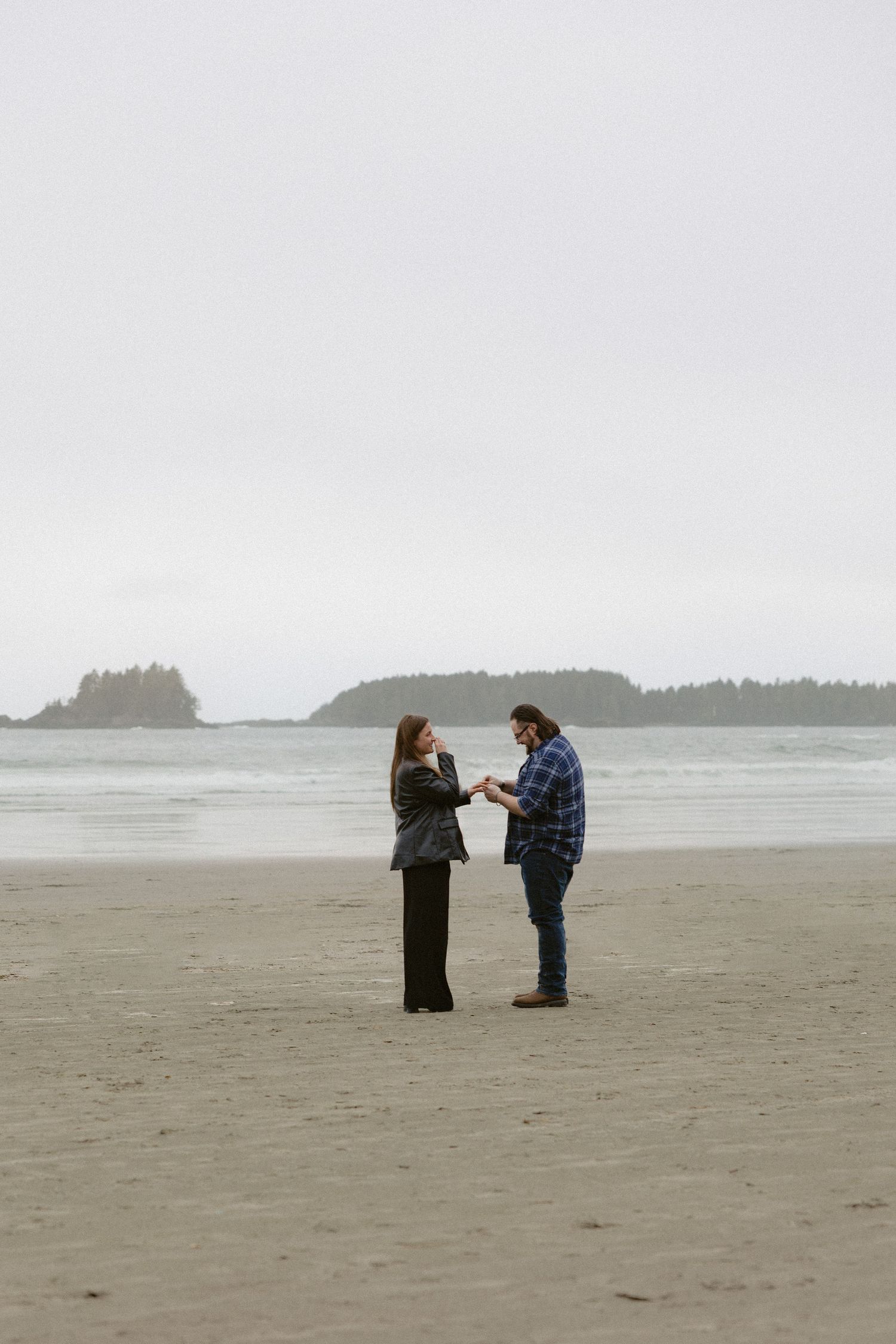 Two people interact on a wide, empty beach with coastal islands visible in the background.