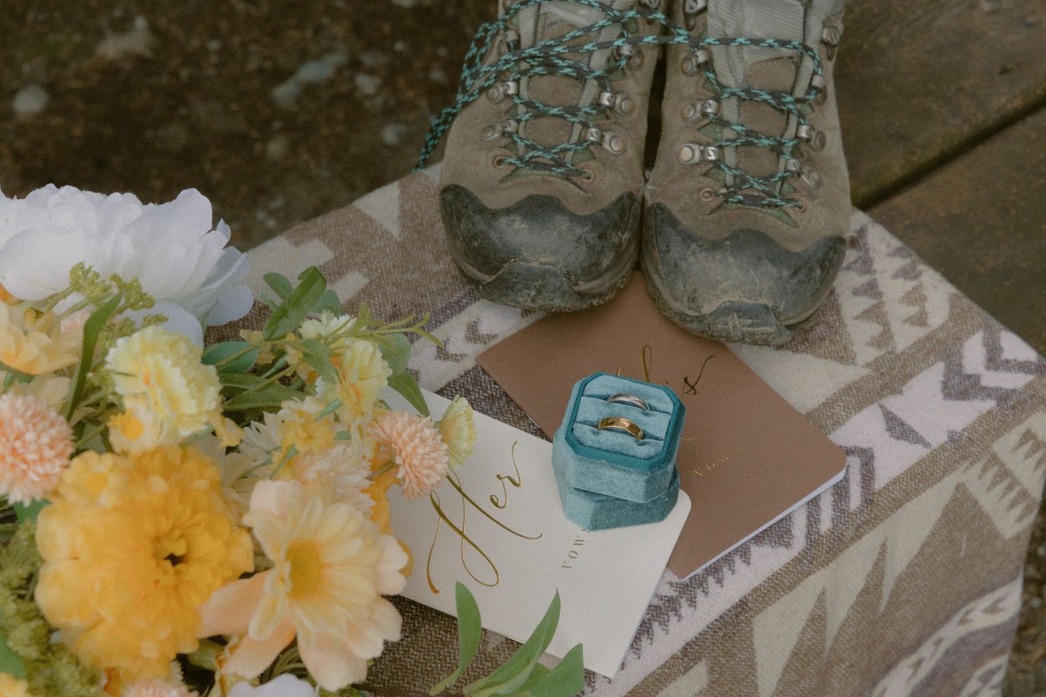 Tofino adventure wedding details on picnic bench including hiking shoes, floral bouquet, vow books, and rings