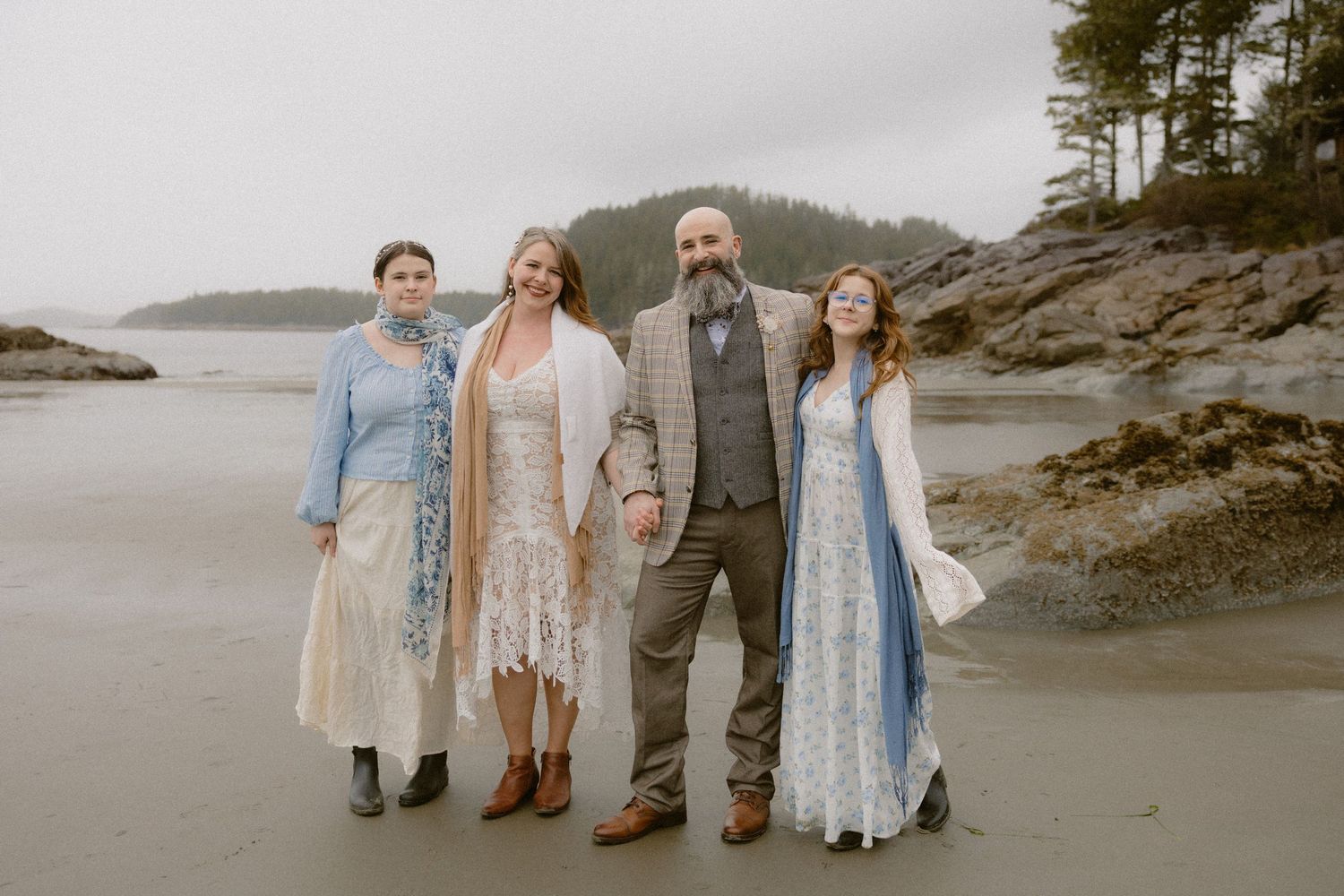 A wedding group poses on a rocky Pacific Northwest beach wearing coordinated blue and white outfits.
