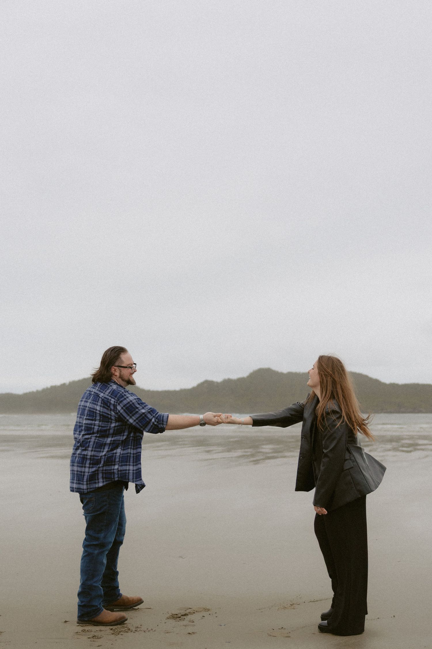 Newly engaged couple dancing on a moody Pacific Northwest beach near Ucluelet
