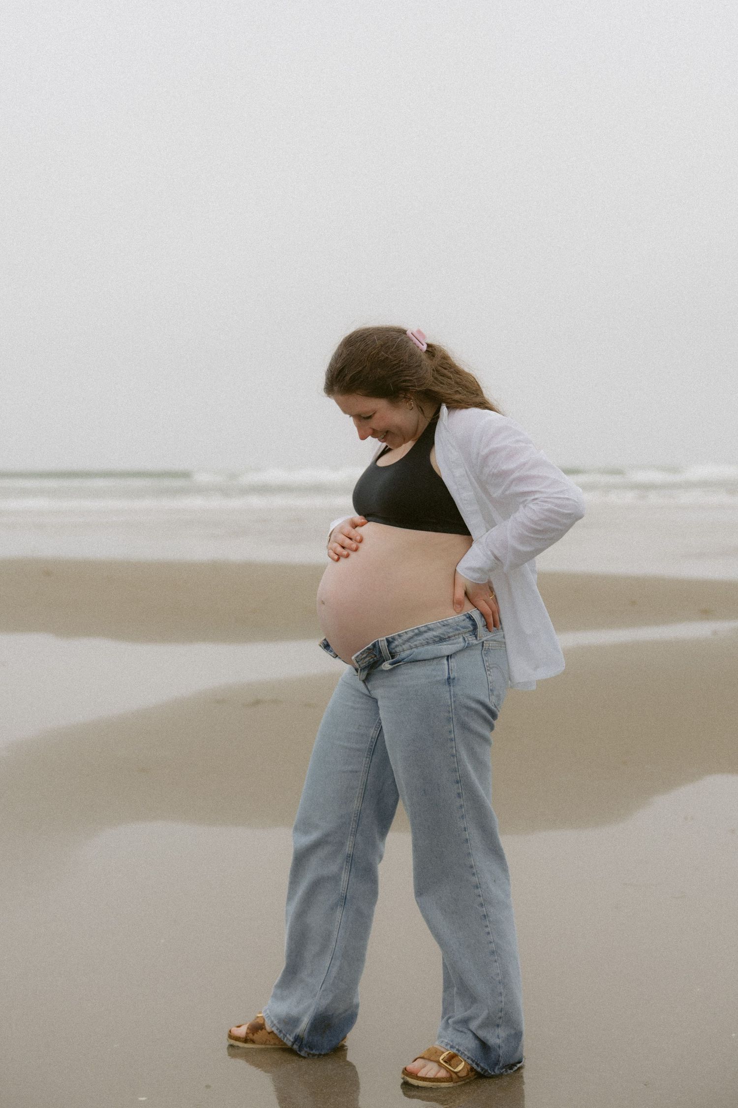 Two people in casual denim outfits embrace while standing on a foggy beach.