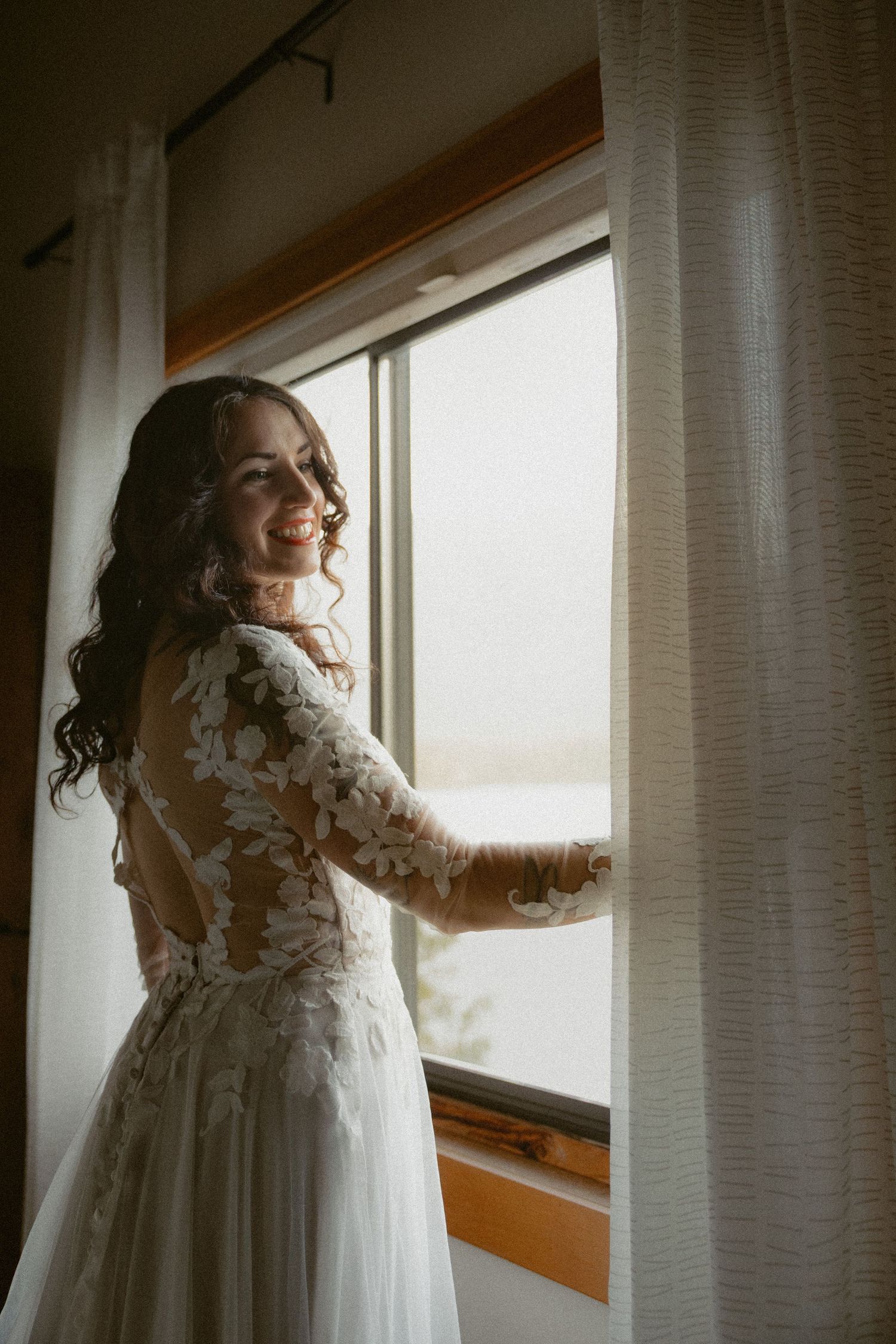 White lace wedding dress flowing gracefully by sunlit windows in a rustic room.