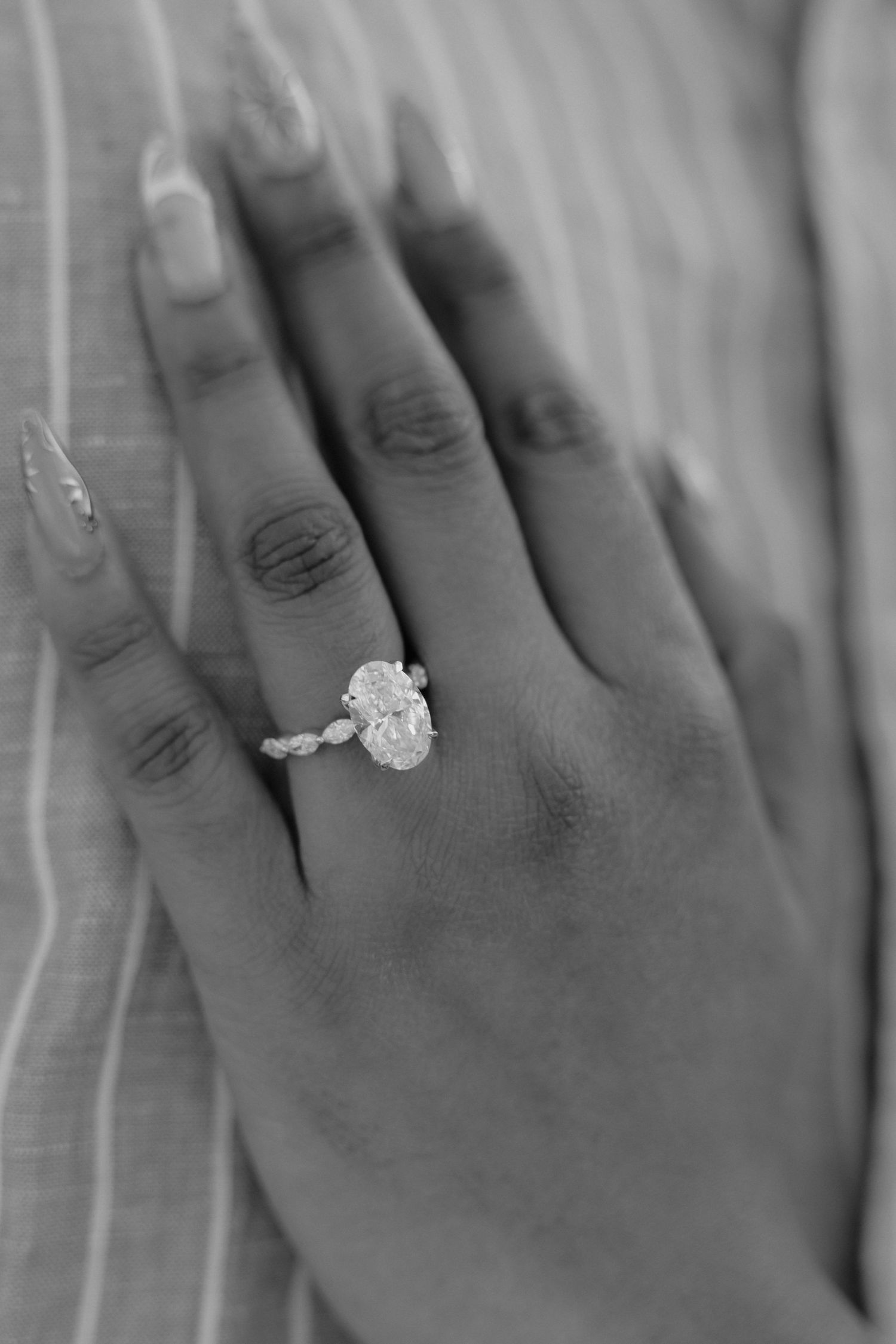 Close-up black and white photo of an oval diamond engagement ring on a woman's hand.