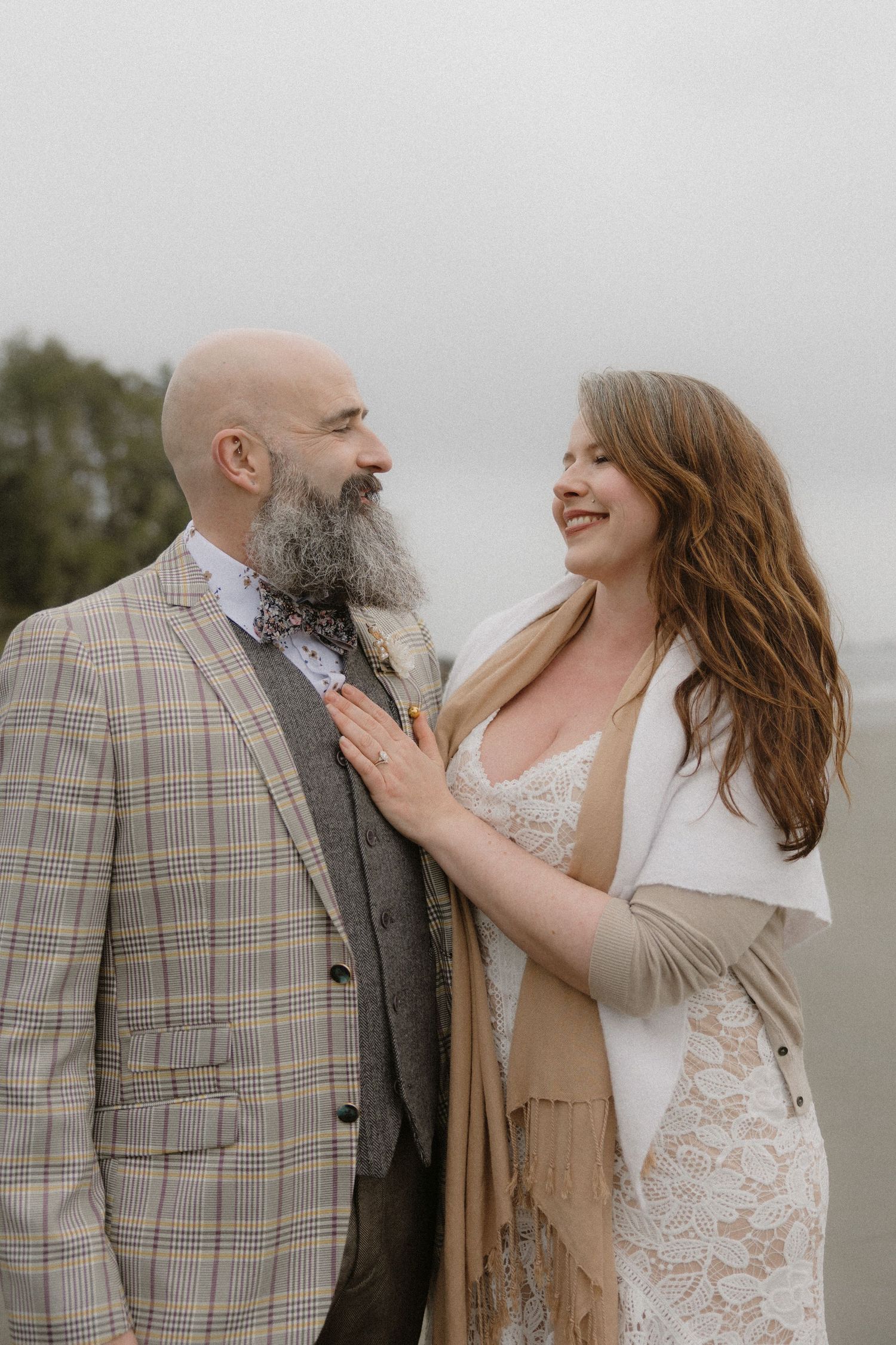 A couple shares a joyful moment on a cloudy beach wearing formal attire.