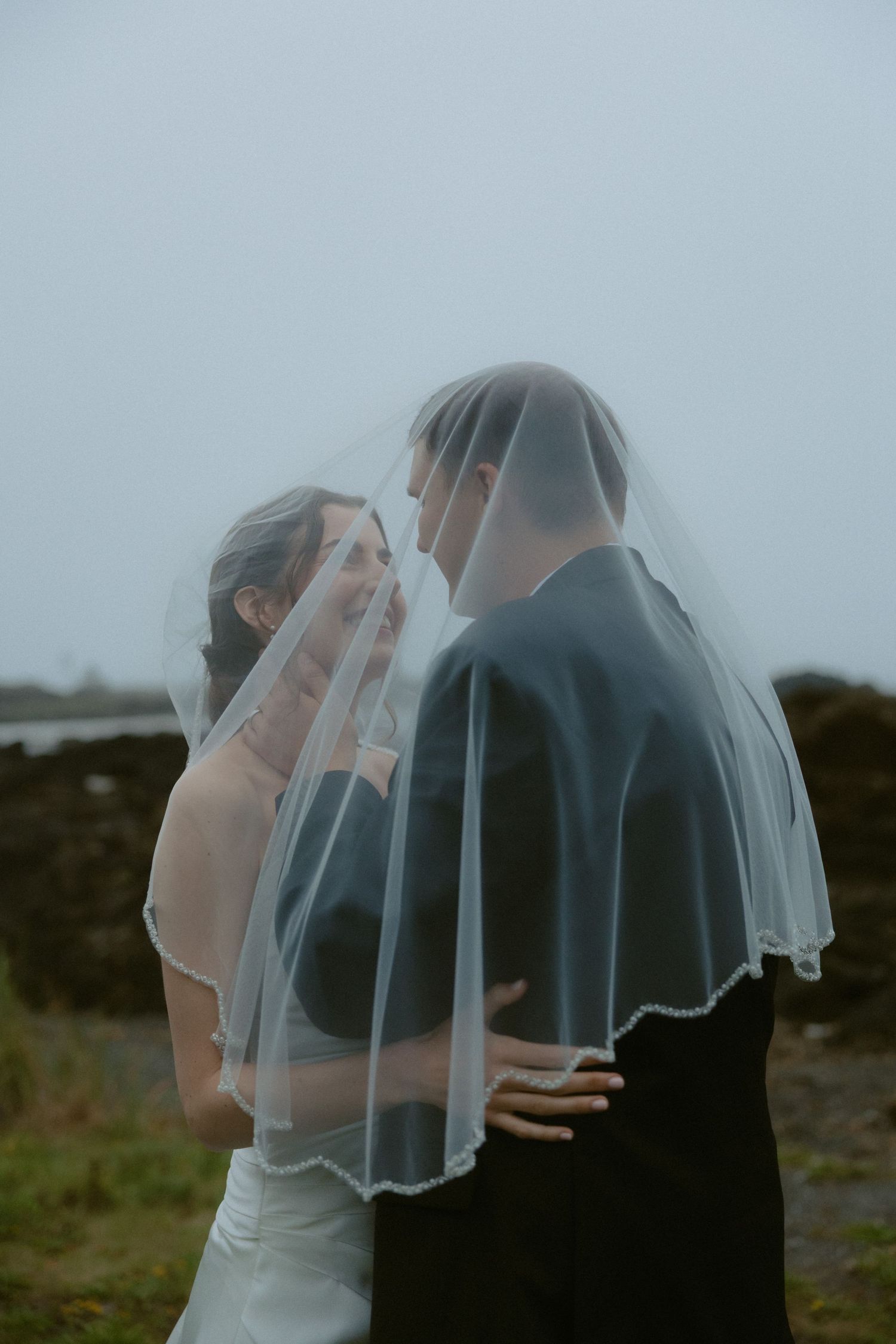 Bride and groom sharing an intimate moment together under a flowing white wedding veil outdoors.