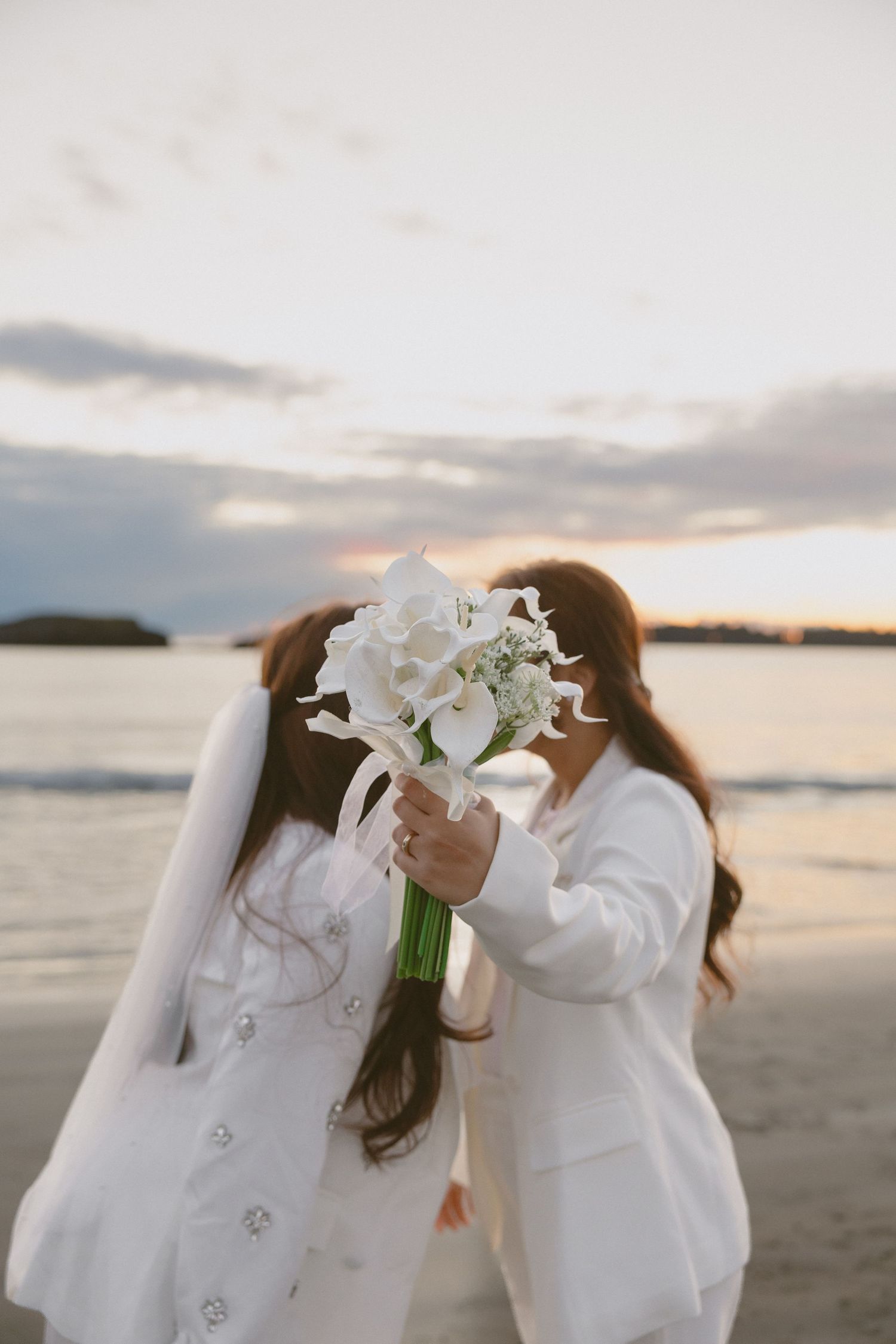 White floral bouquets held against a beach sunset backdrop creating a romantic silhouette.