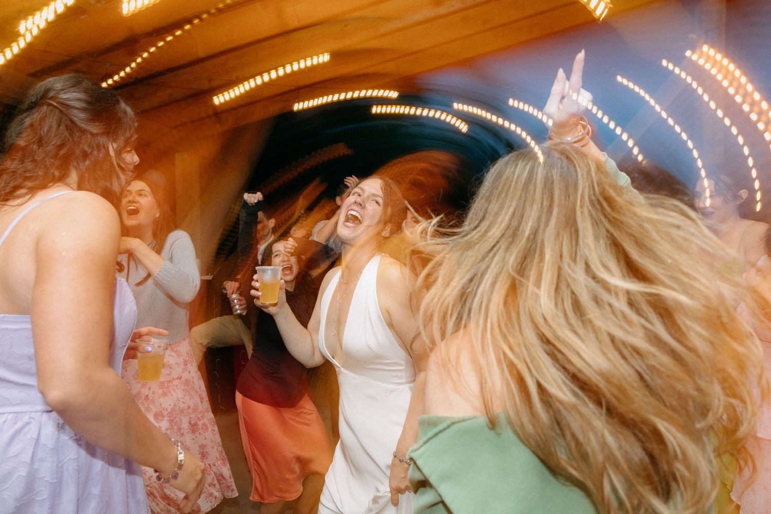 Group of young women dancing and laughing at a carnival fairground at night with bright lights.