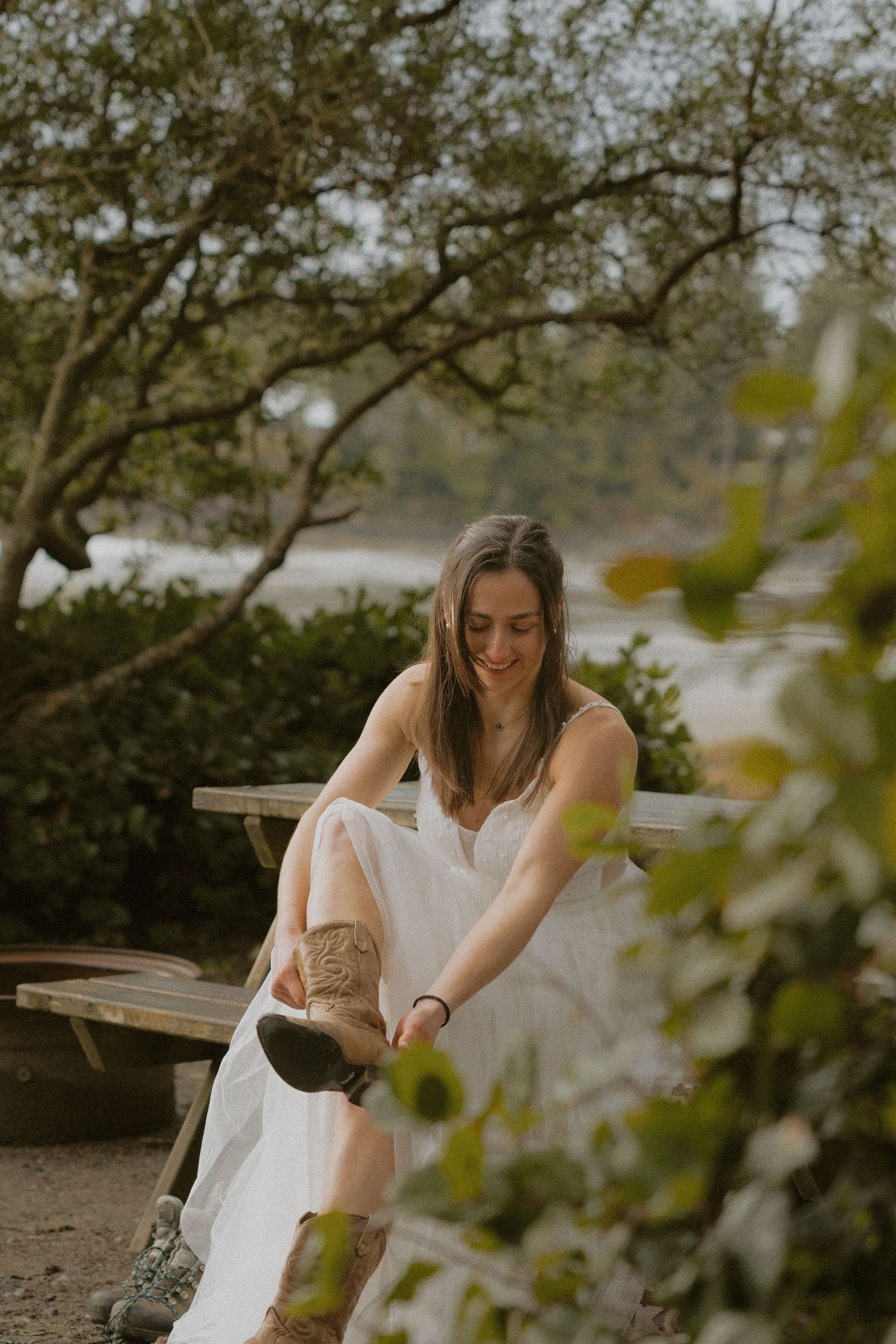 Ucluelet elopement bride in white dress putting on her boots at Bella Pacifica Campground rustic wooden bench