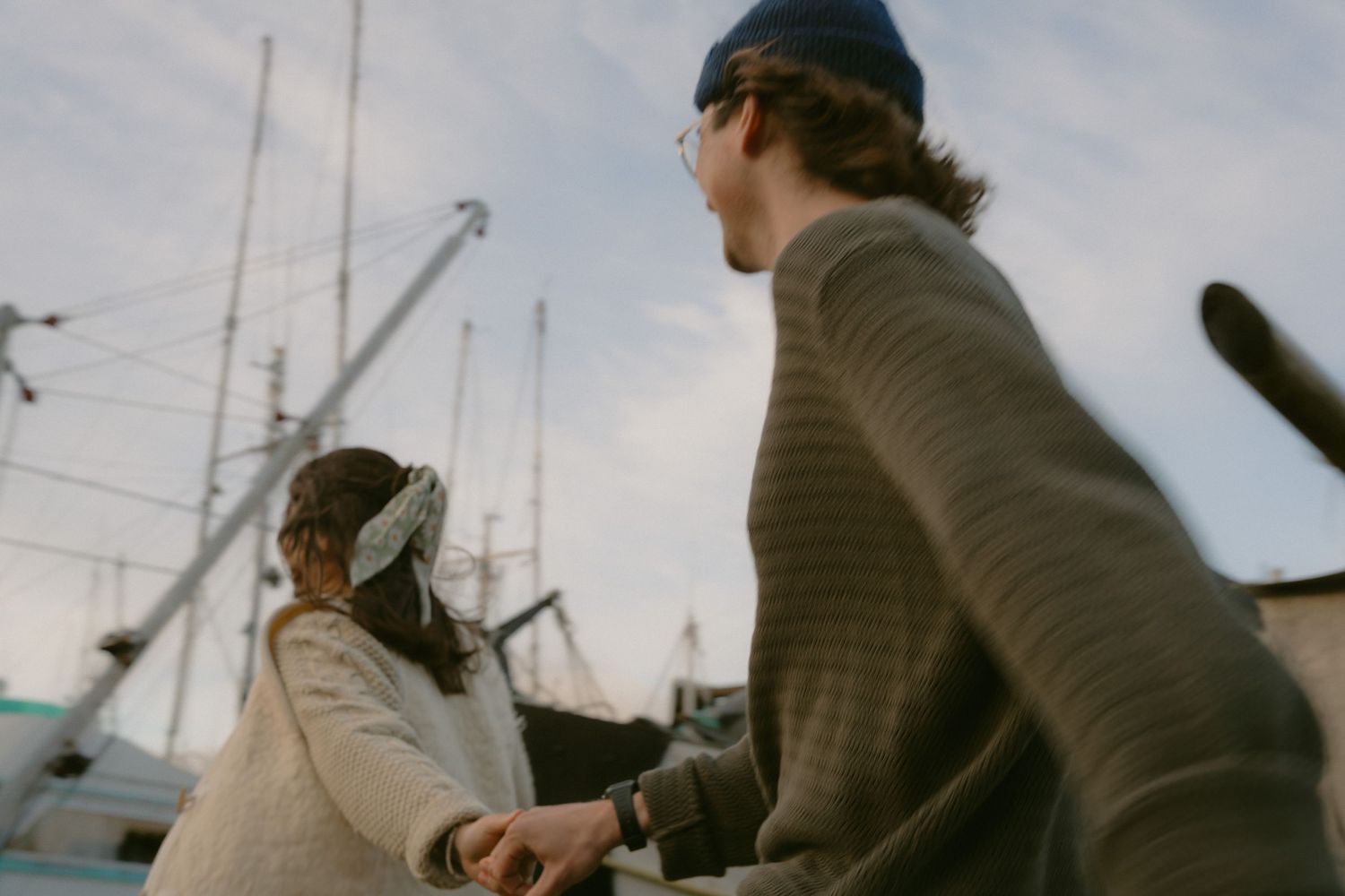 A couple walks together along a marina dock with moored boats visible in the background.