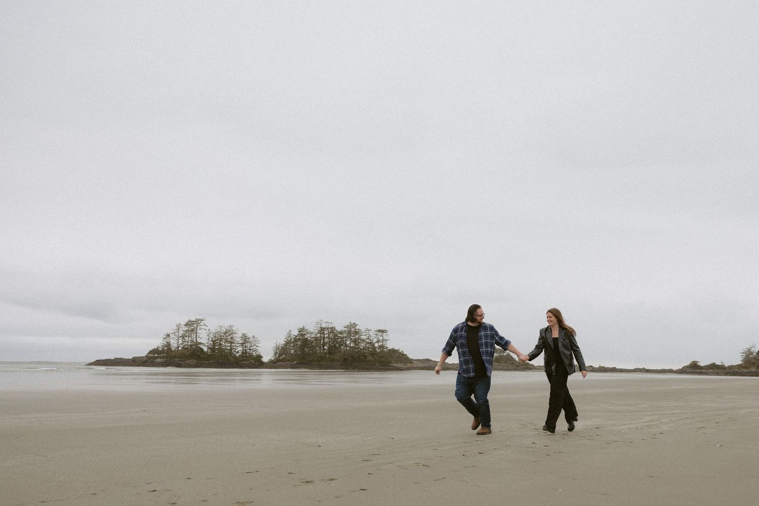 Distant figures walking together on a foggy Pacific Northwest beach with mountains in background.