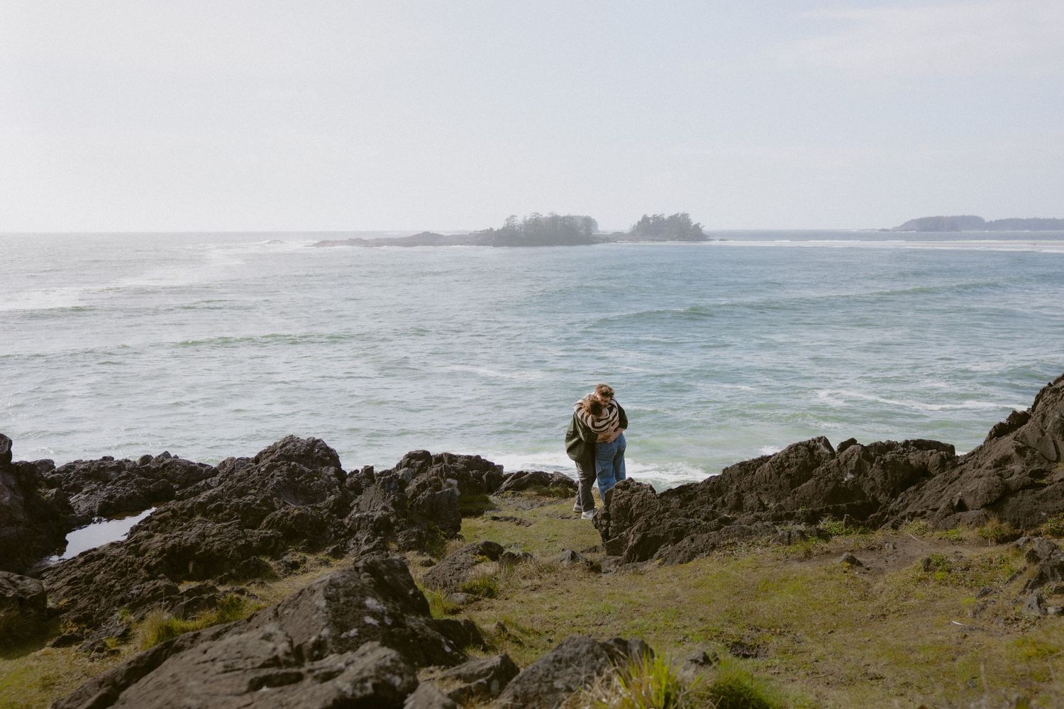 Hiker with backpack standing on rocky coastal shoreline overlooking calm ocean waters.