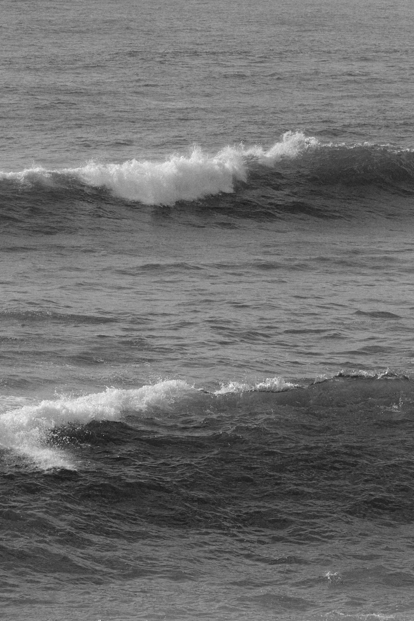 Black and white ocean waves crashing with white foam on dark choppy sea water.