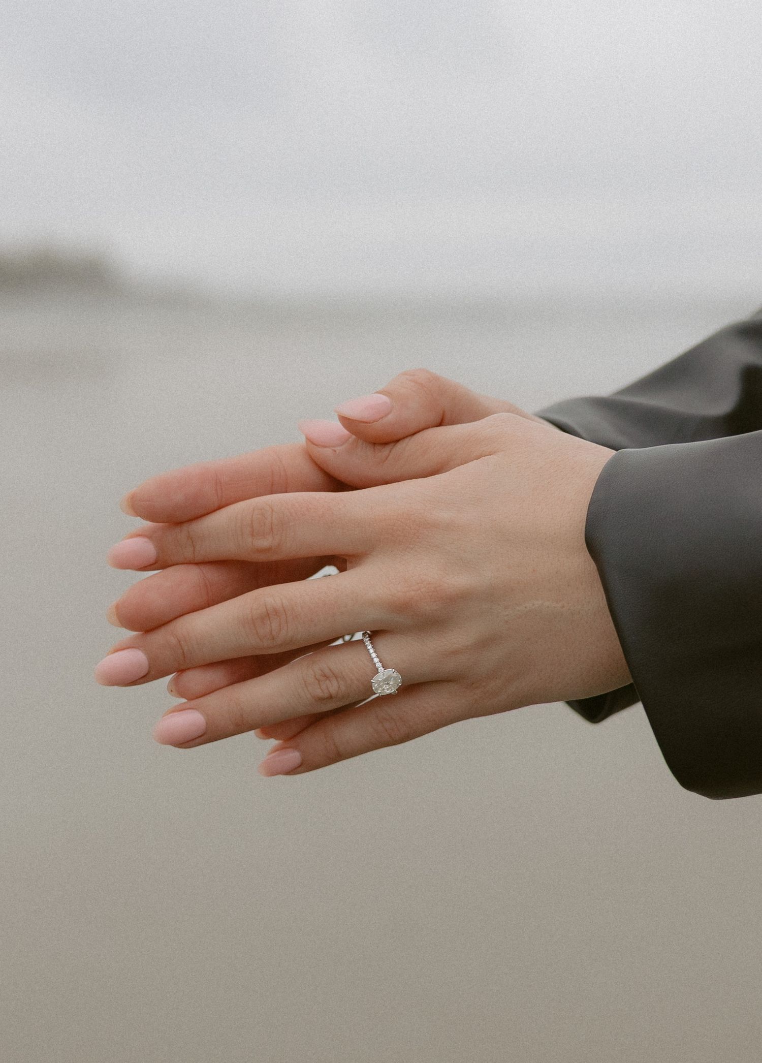 Close-up of hands with engagement ring against Chesterman Beach Tofino