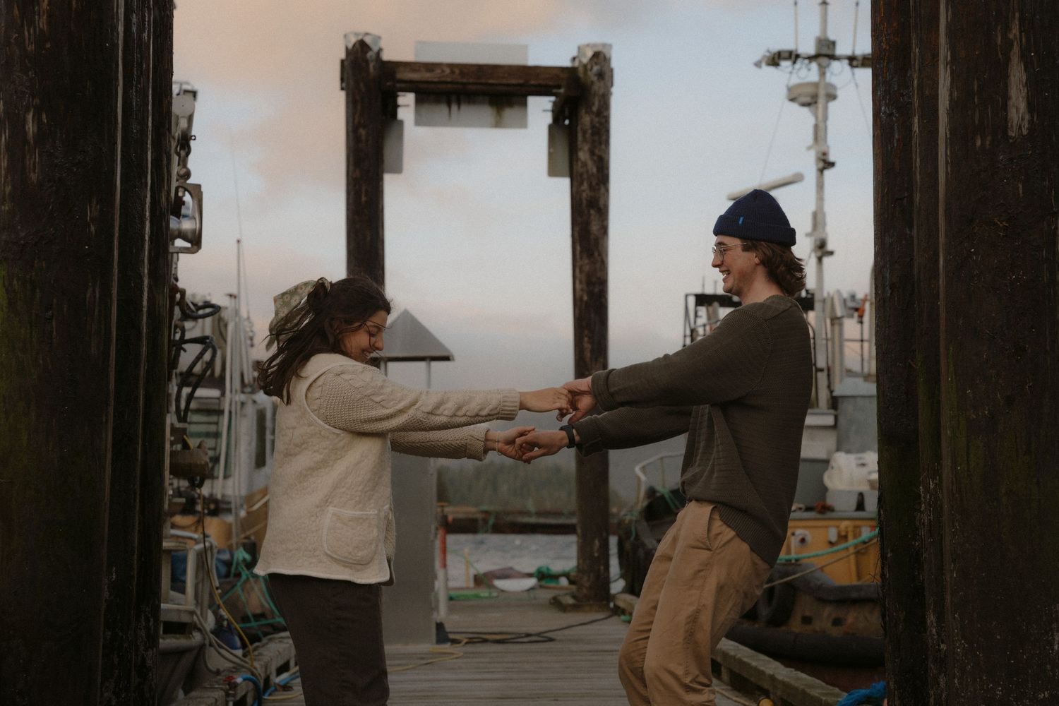 Two individuals share a moment on a dock surrounded by marina posts and boats.