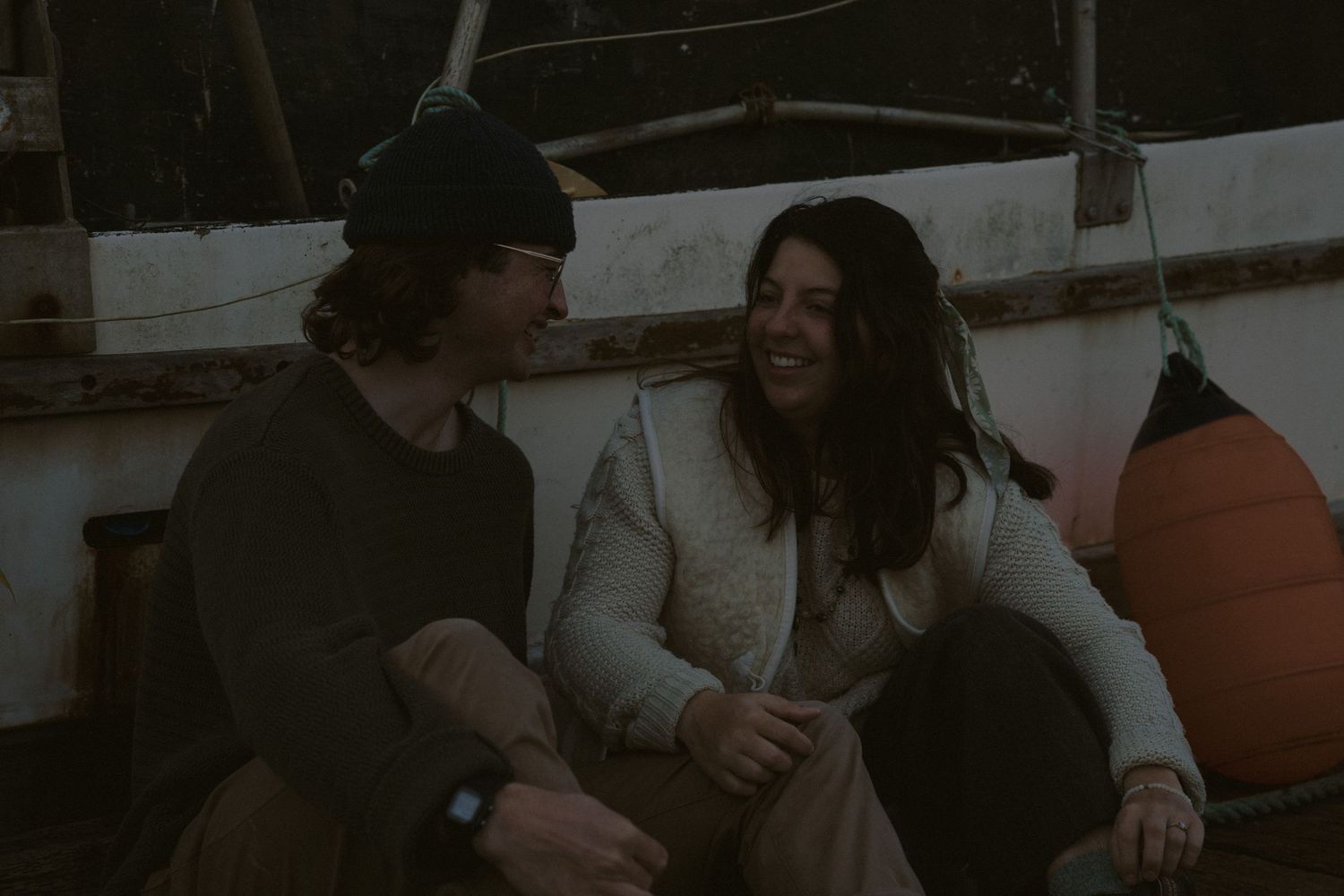 Couple relaxing on dock surrounded by boats at dusk.