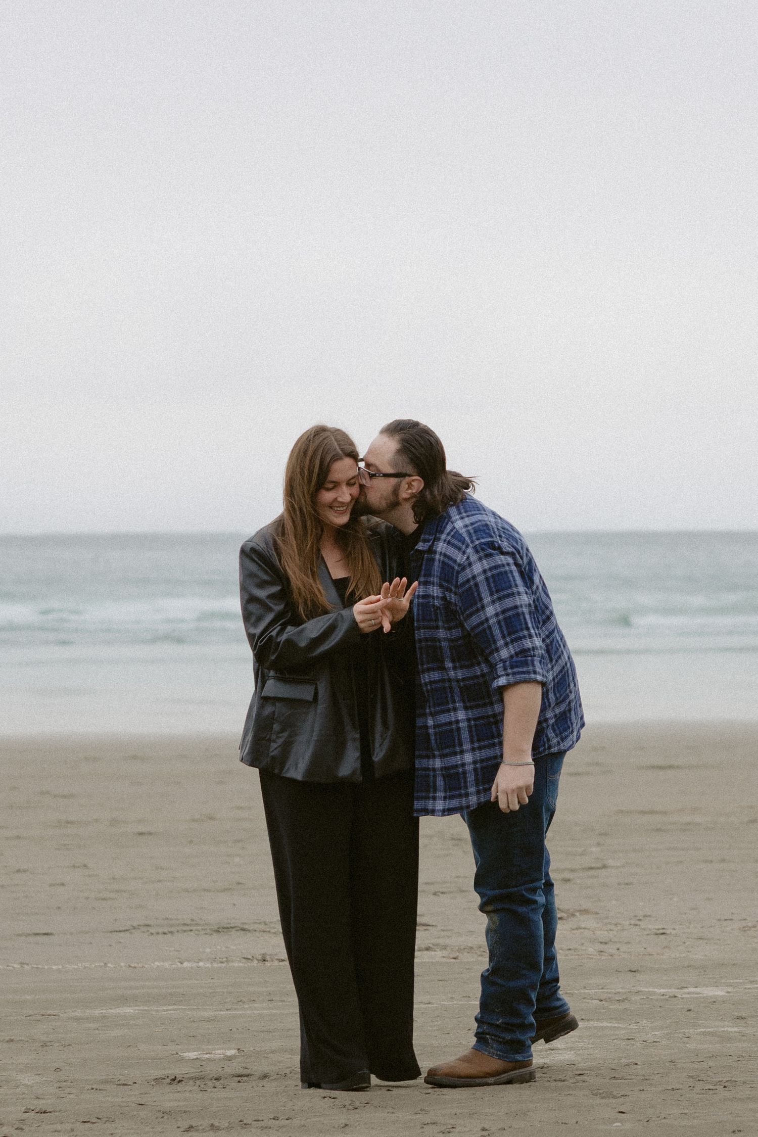 An intimate moment captured between two people on a cloudy beach.