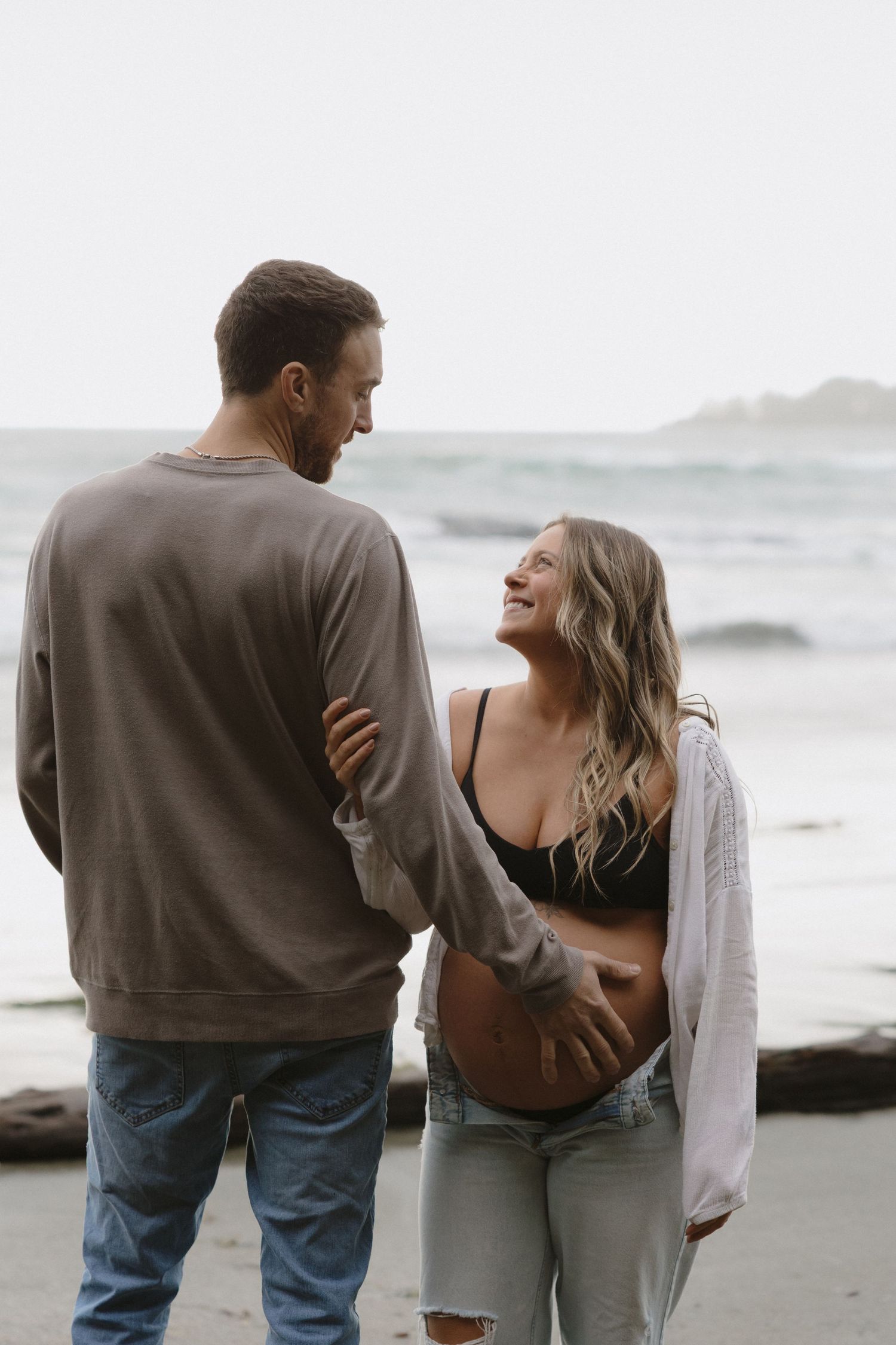 Intimate maternity photo of couple sharing a joyful moment on rocky beach.