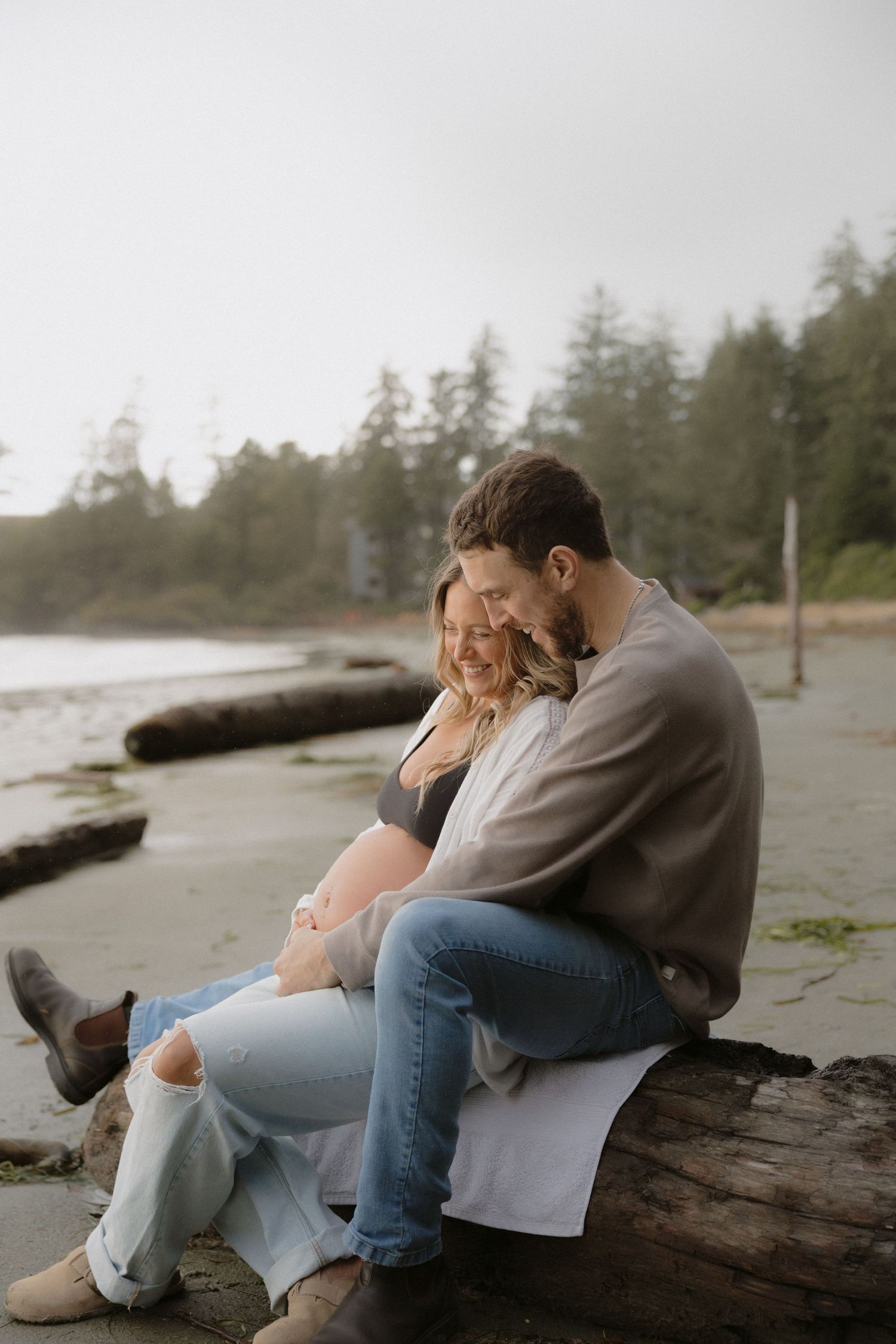 Couple sits together on driftwood at a foggy beach.