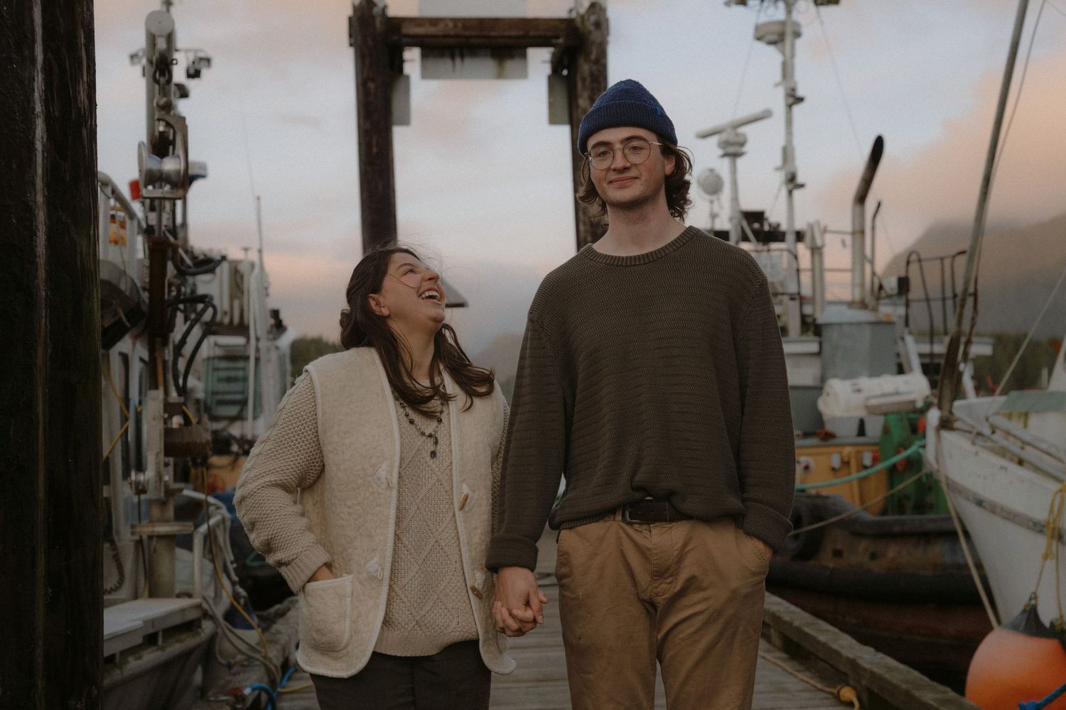 People interact on a wooden pier with boats and nautical equipment in the background.