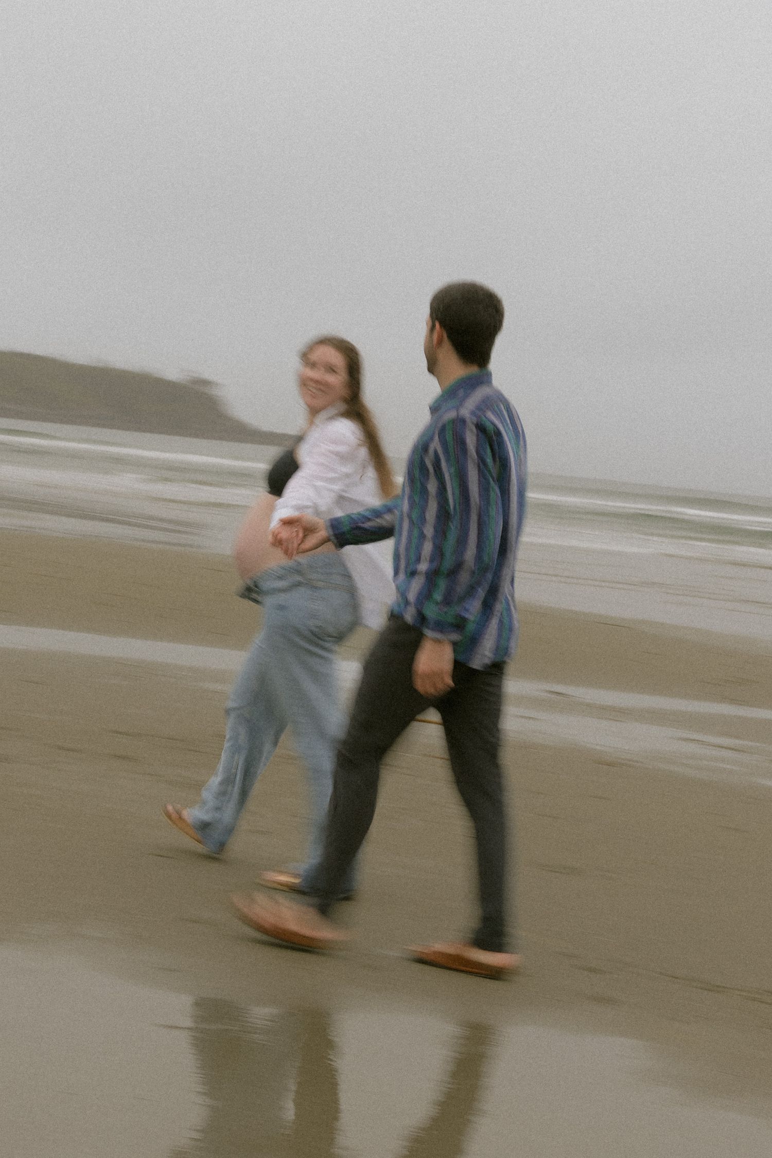 A couple dances playfully together on a misty beach during low tide.
