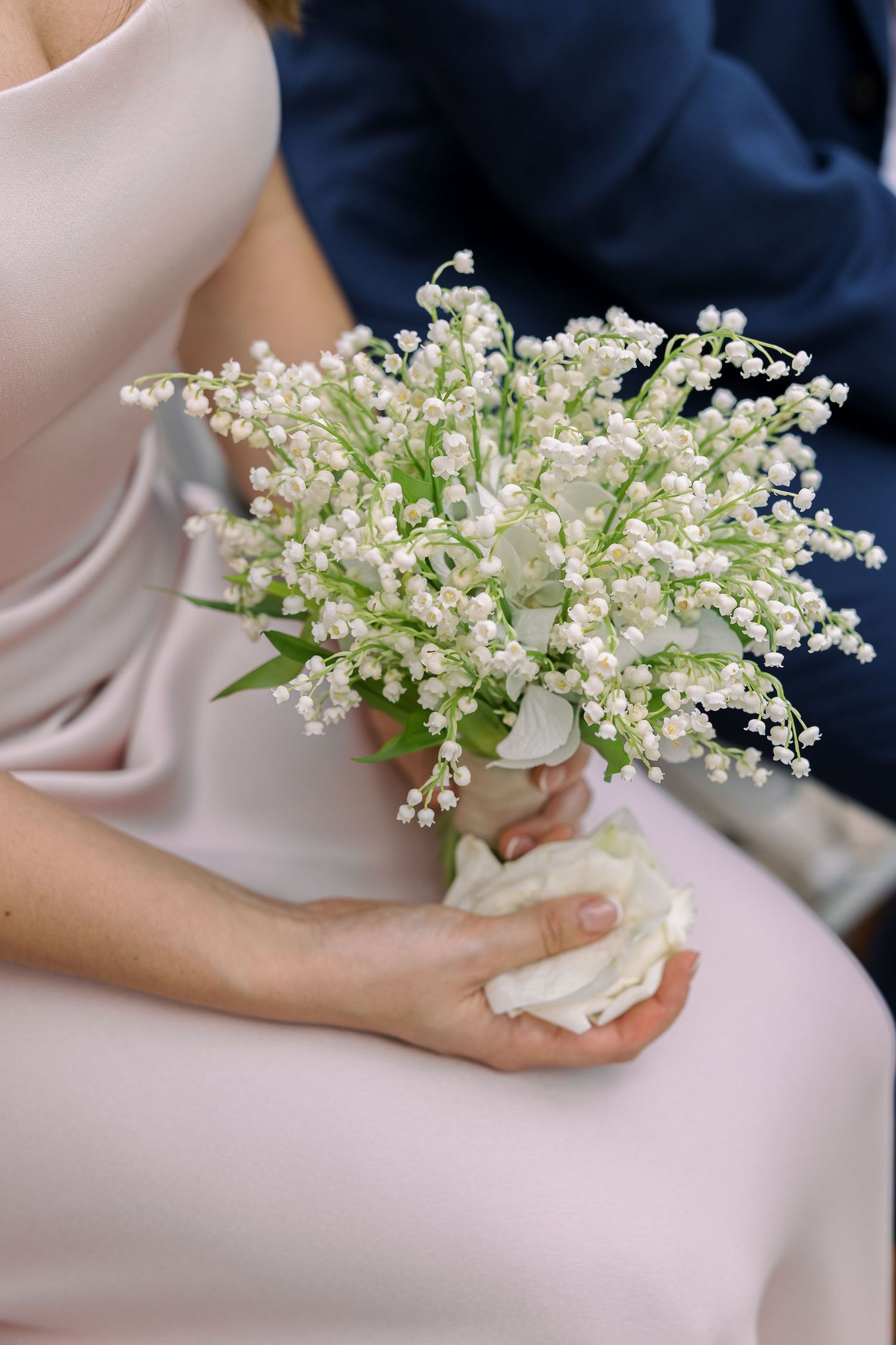 Bride holding a delicate lily of the valley wedding bouquet in white, paired with a blush pink dress.