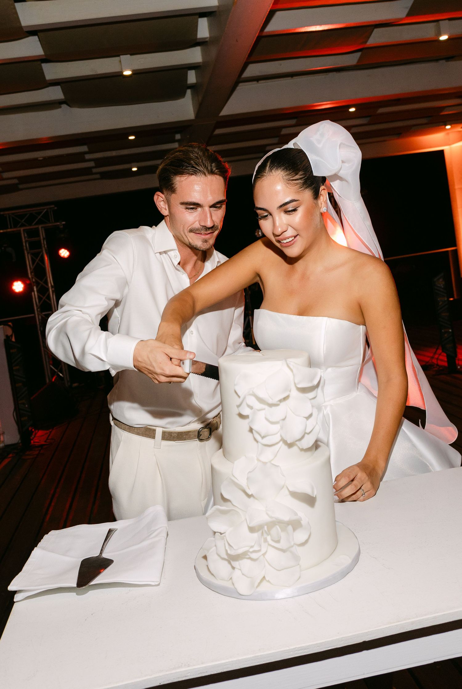 A wedding couple cutting their elegant white tiered cake together at their reception.