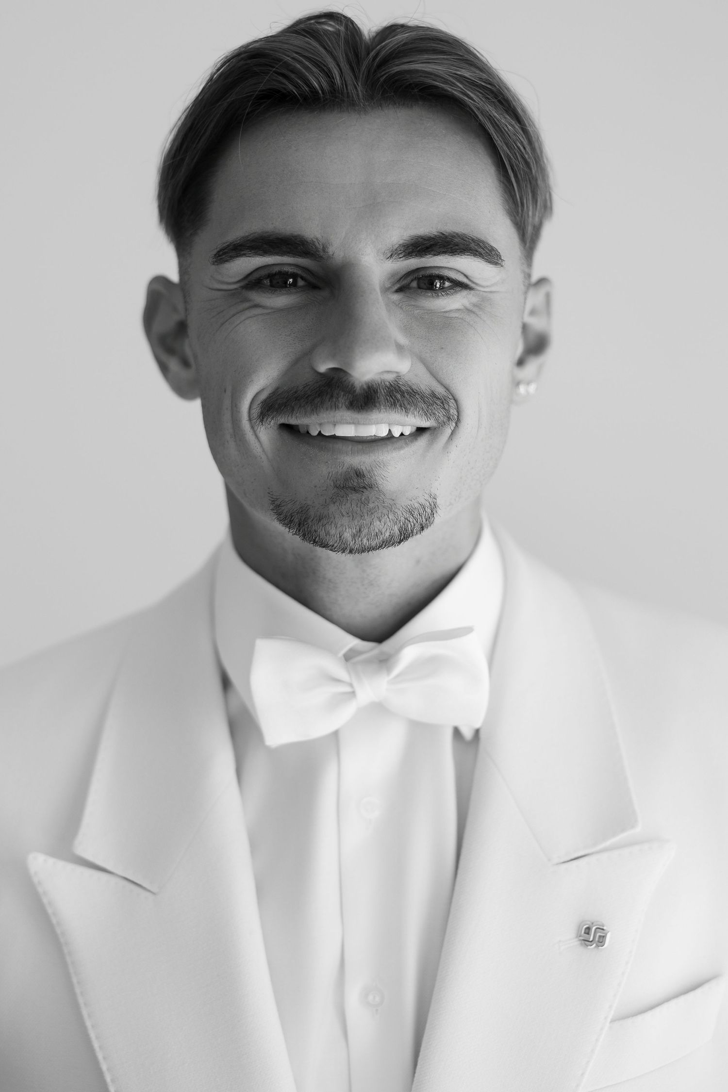 Black and white portraits of groom in white tuxedo and bowtie.
