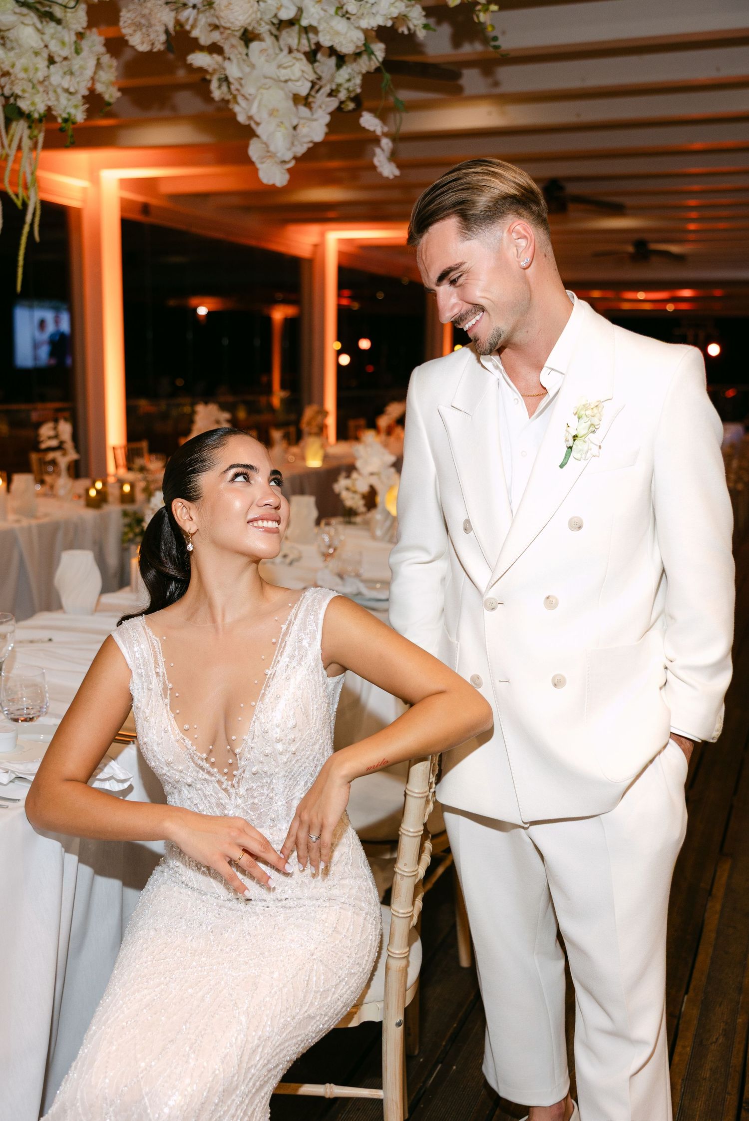 Wedding couple dancing and laughing together at their reception with white floral decorations overhead.