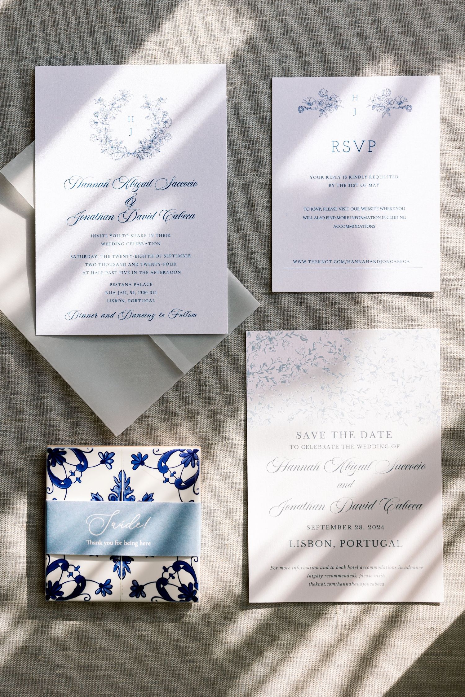 Wedding invitation suite with blue floral design and elegant typography on gray linen background.