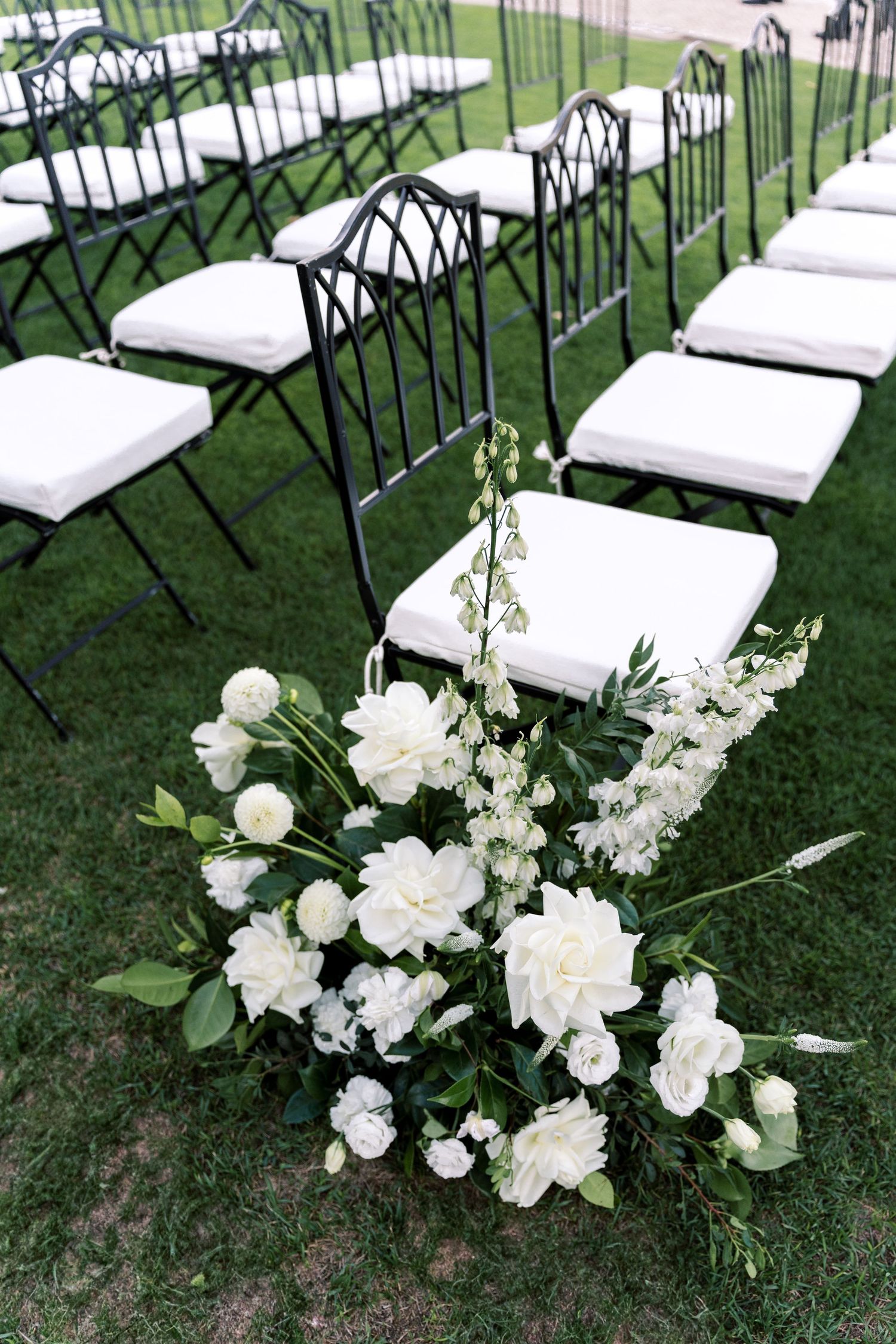 Outdoor wedding ceremony setup with white chairs and floral arrangements on grass.